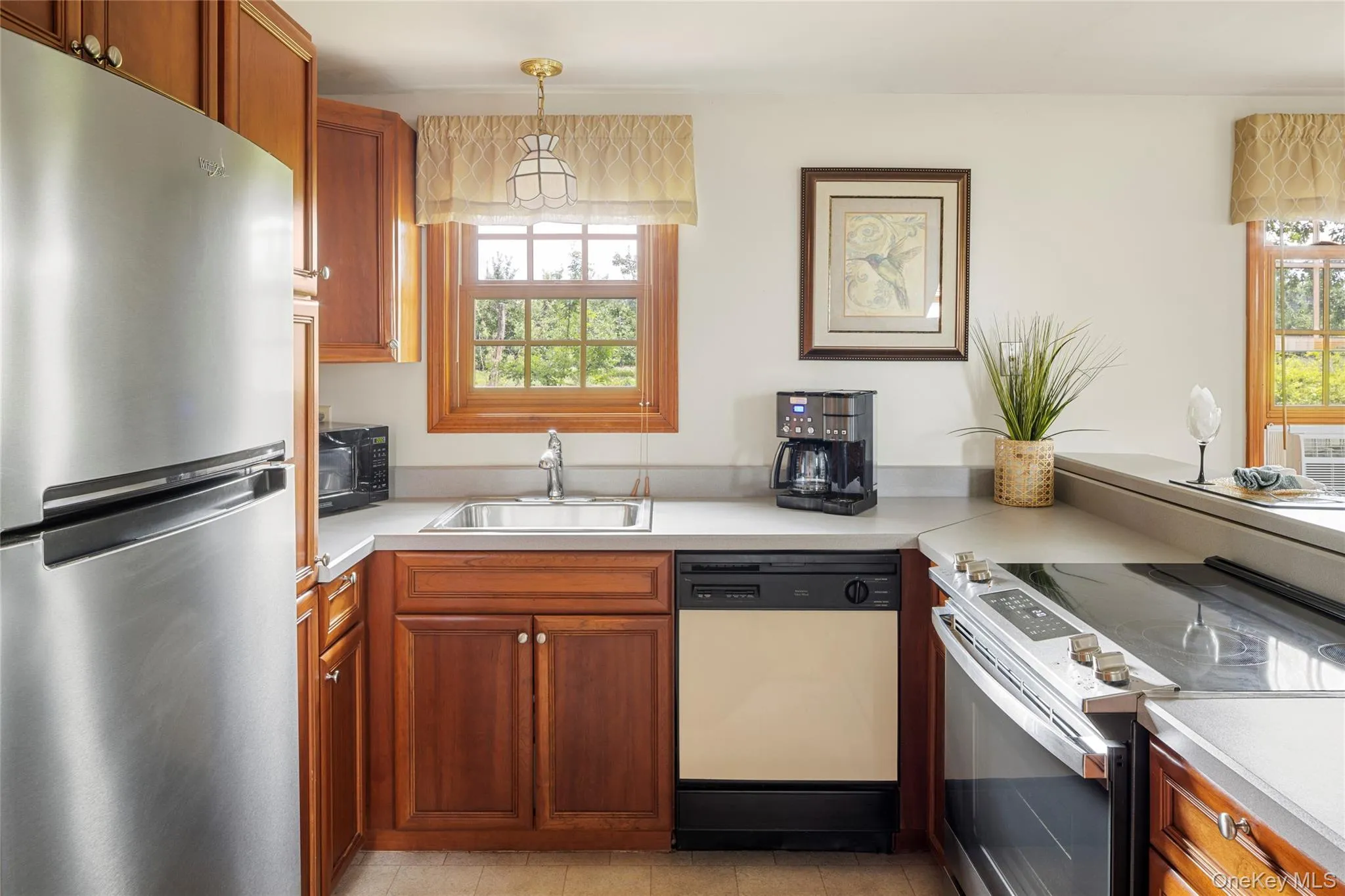 Kitchen with stainless steel appliances, light countertops, hanging light fixtures, and brown cabinetry Kitchen with stainless steel appliances, light countertops, hanging light fixtures, and brown cabinetry