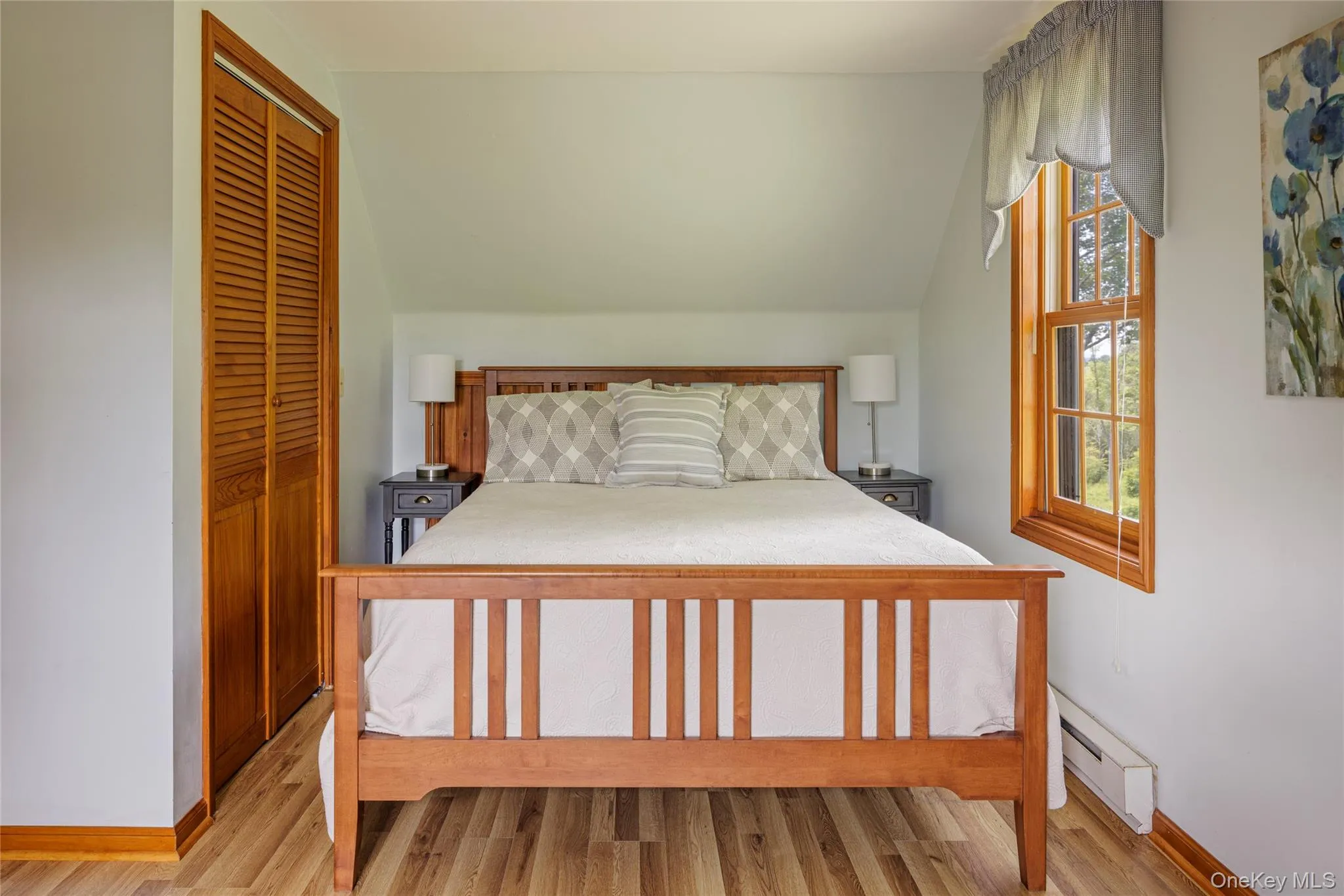 Bedroom featuring baseboard heating, light wood finished floors, and a closet Bedroom featuring baseboard heating, light wood finished floors, and a closet