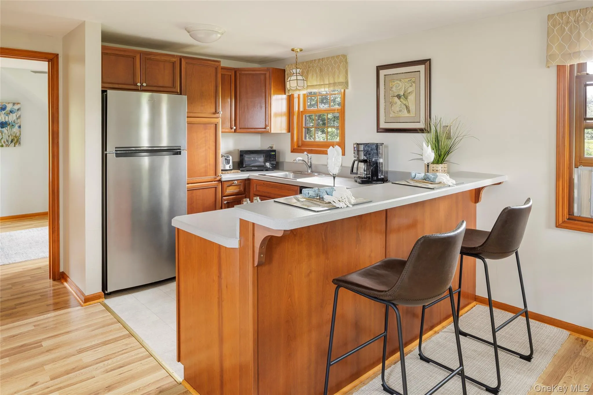 Kitchen featuring freestanding refrigerator, a peninsula, brown cabinetry, light countertops, and black microwave Kitchen featuring freestanding refrigerator, a peninsula, brown cabinetry, light countertops, and black microwave