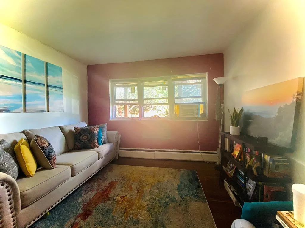 Living area featuring a baseboard heating unit, wood finished floors, and cooling unit Living area featuring a baseboard heating unit, wood finished floors, and cooling unit