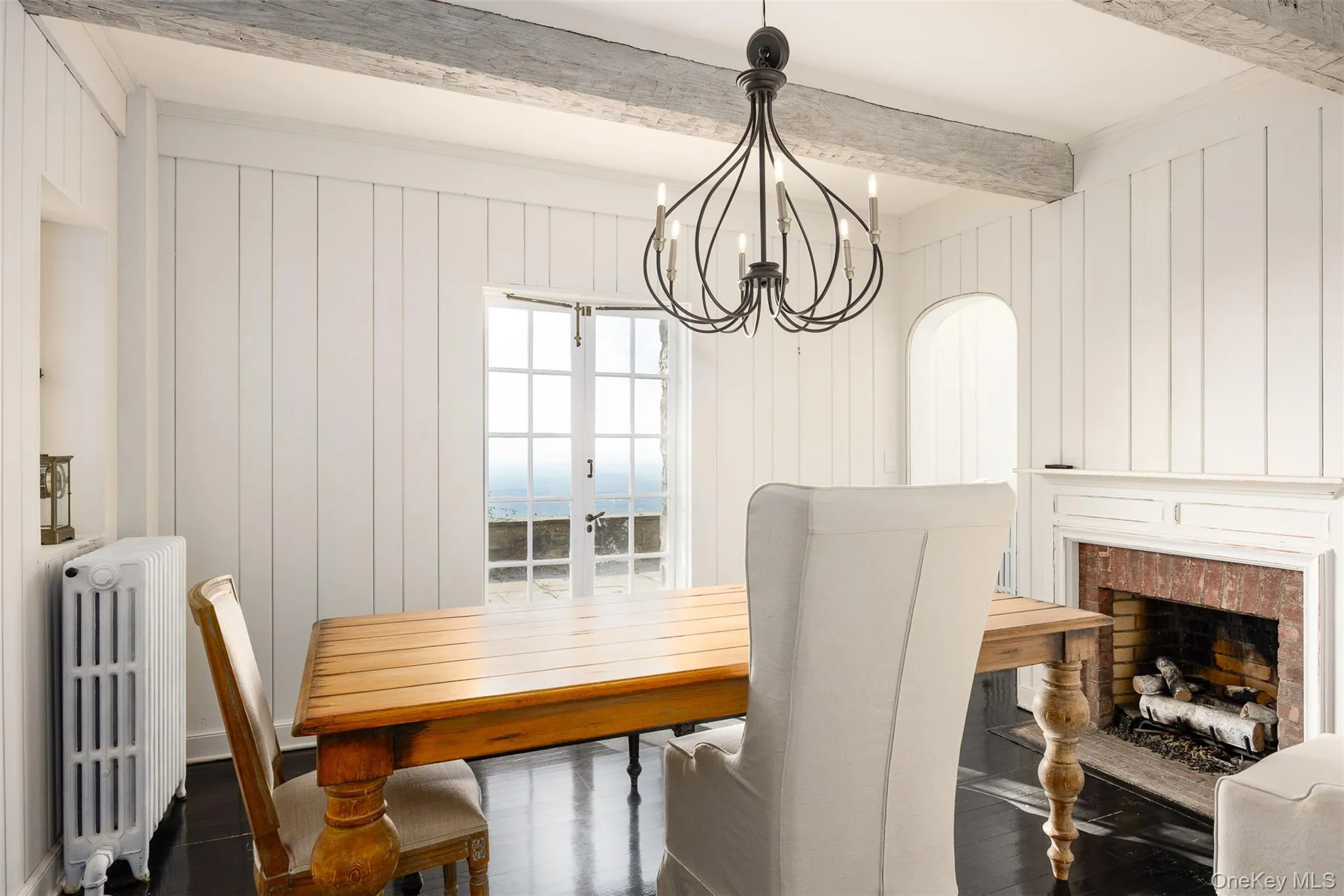 Dining room featuring radiator heating unit, beamed ceiling, a chandelier, wood finished floors, and a decorative wall Dining room featuring radiator heating unit, beamed ceiling, a chandelier, wood finished floors, and a decorative wall