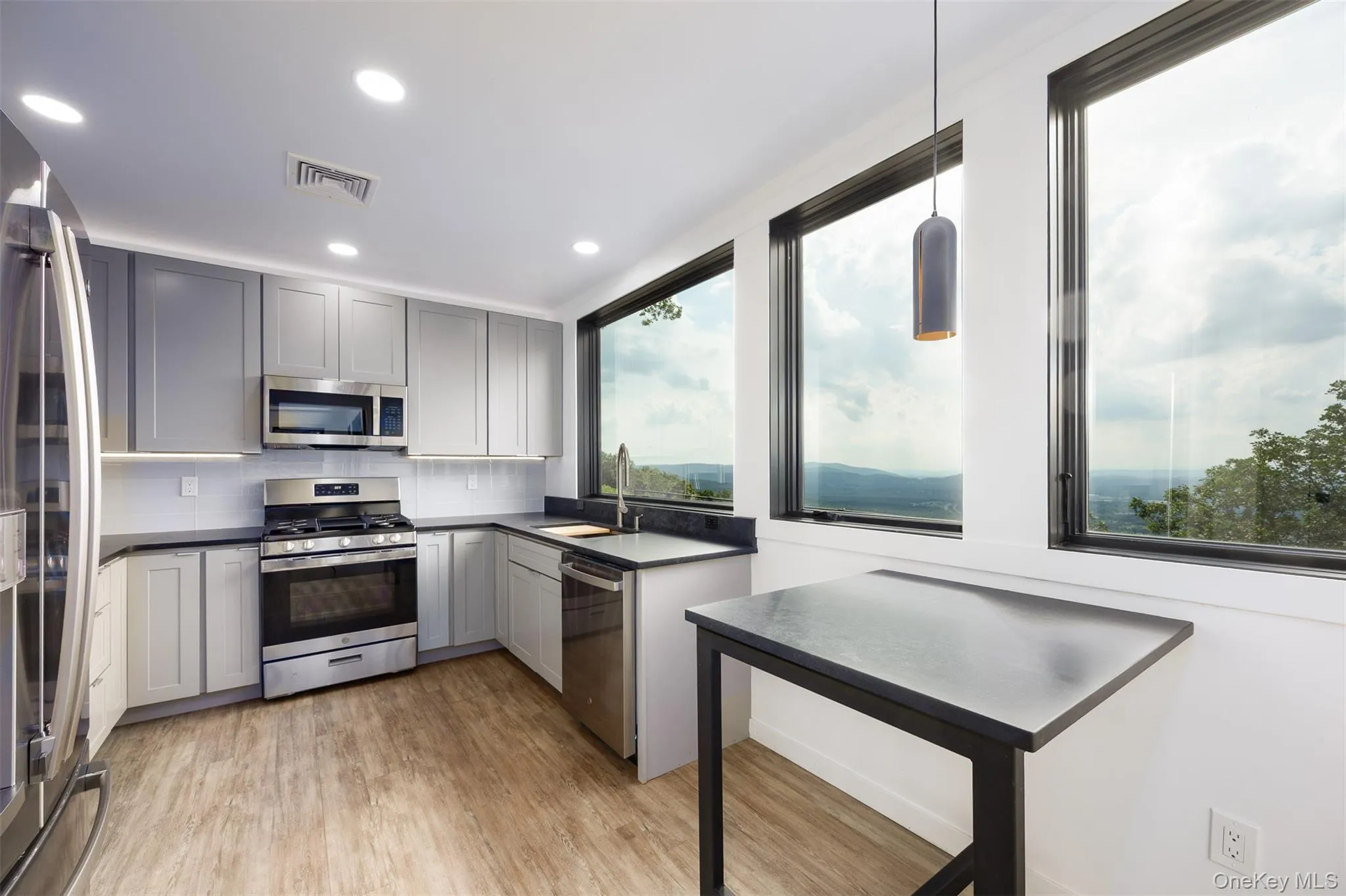 Kitchen featuring dark countertops, appliances with stainless steel finishes, light wood-type flooring, decorative backsplash, and gray cabinets Kitchen featuring dark countertops, appliances with stainless steel finishes, light wood-type flooring, decorative backsplash, and gray cabinets