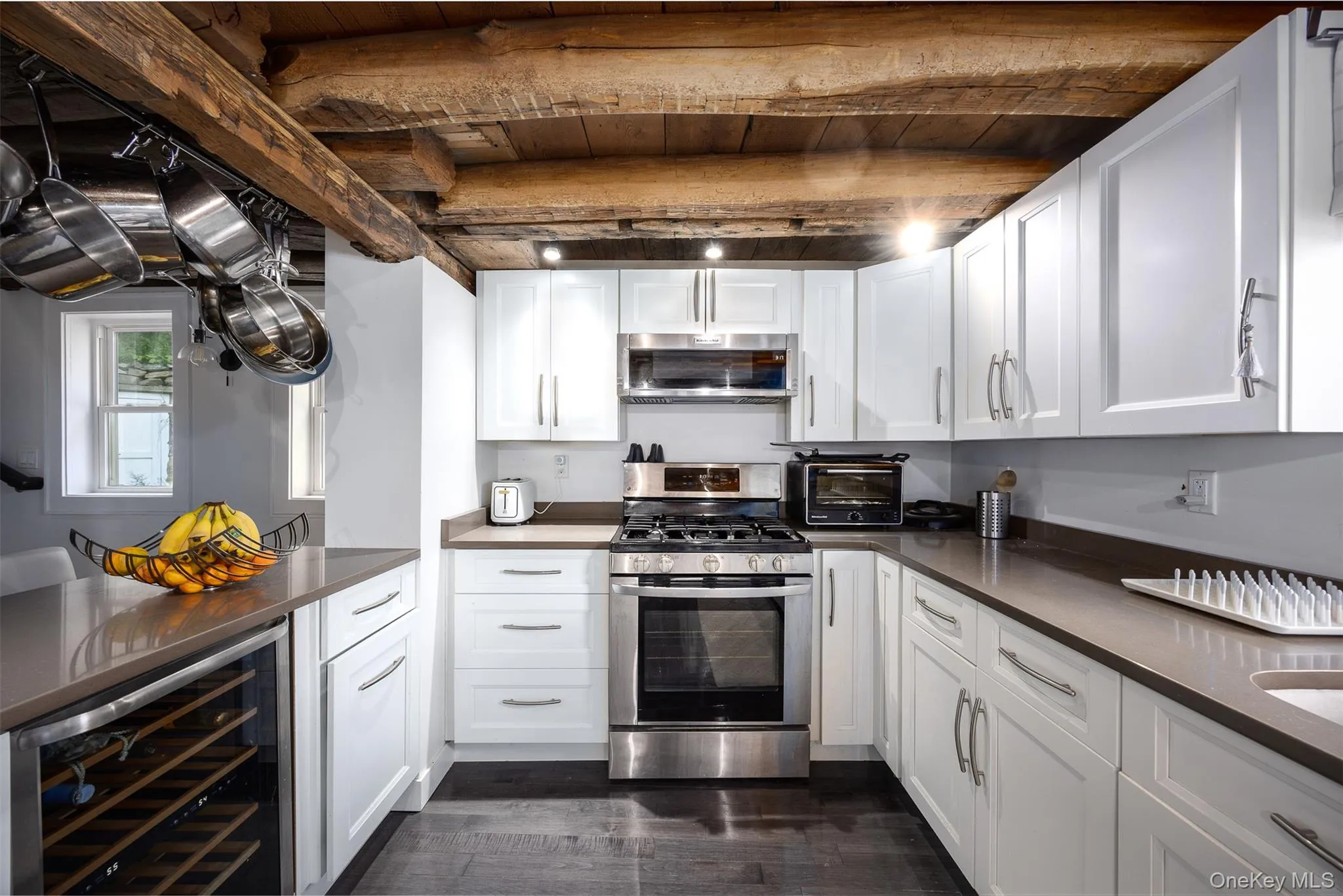 Kitchen with beverage cooler, appliances with stainless steel finishes, dark countertops, dark wood-style flooring, and white cabinets Kitchen with beverage cooler, appliances with stainless steel finishes, dark countertops, dark wood-style flooring, and white cabinets