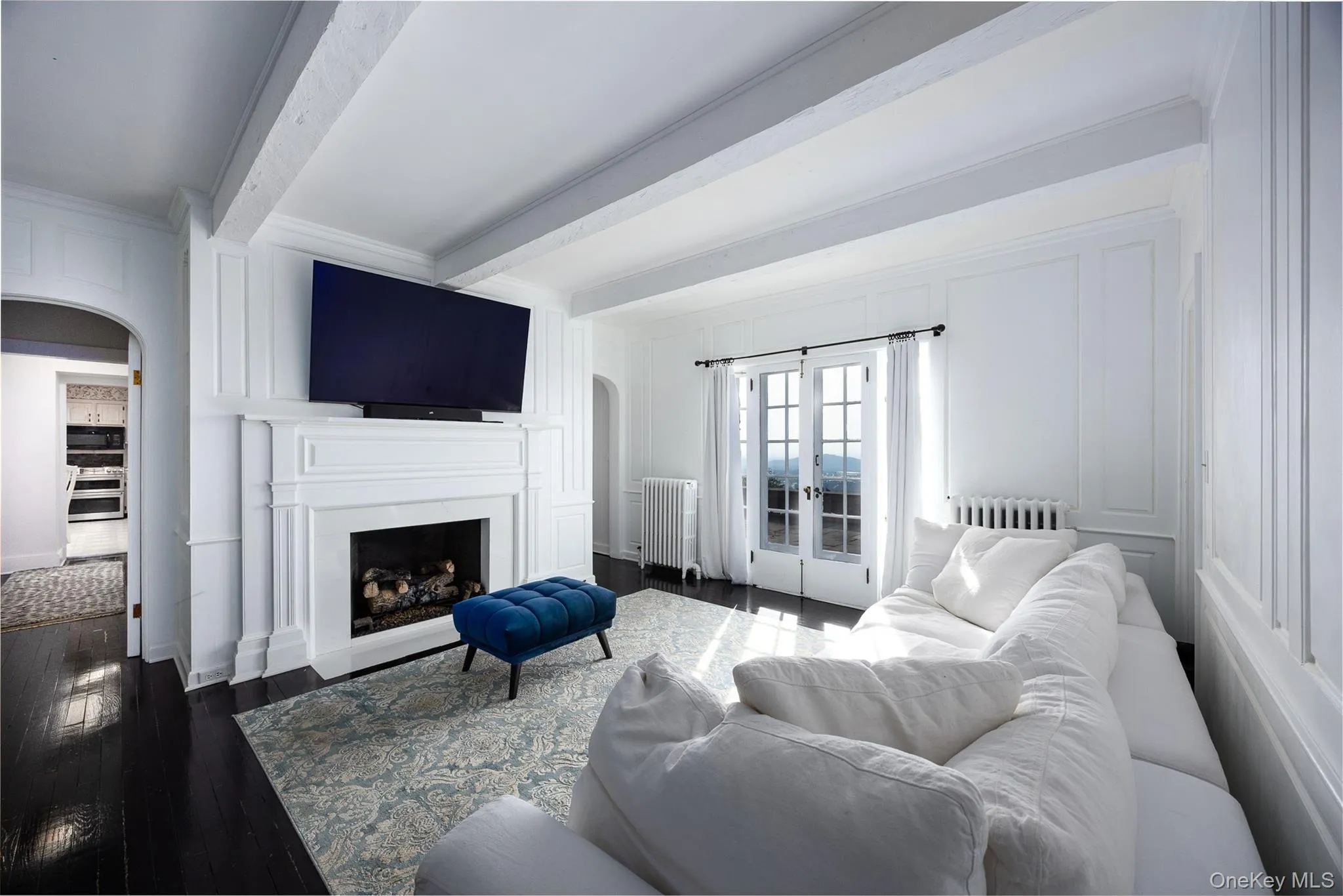 Living room featuring french doors, arched walkways, beamed ceiling, wood finished floors, and radiator heating unit Living room featuring french doors, arched walkways, beamed ceiling, wood finished floors, and radiator heating unit