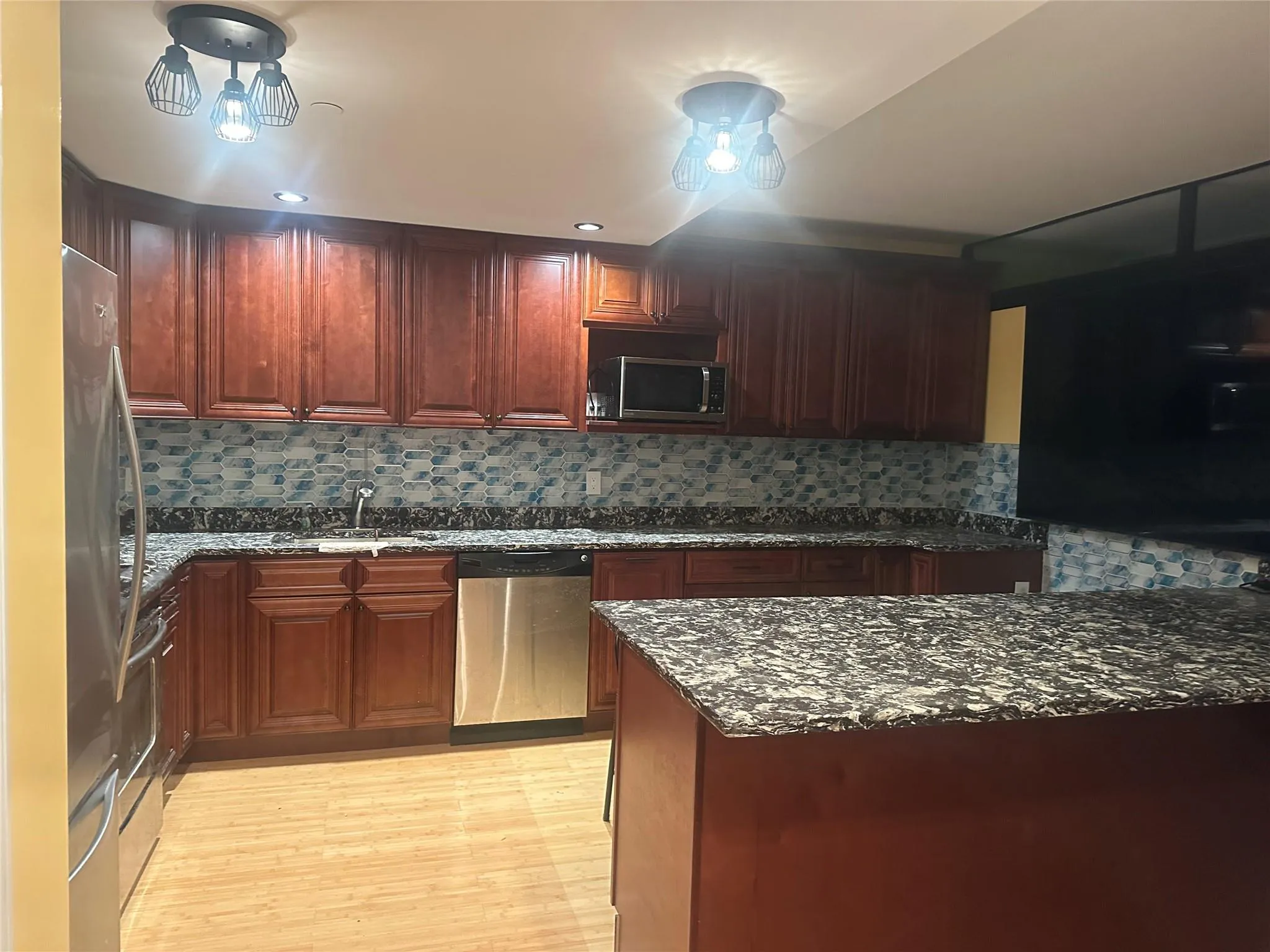 Kitchen featuring stainless steel appliances, dark stone countertops, light wood-style floors, backsplash, and dark brown cabinets Kitchen featuring stainless steel appliances, dark stone countertops, light wood-style floors, backsplash, and dark brown cabinets