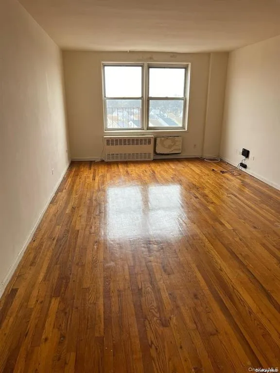 Unfurnished room with hardwood / wood-style floors and radiator Unfurnished room with hardwood / wood-style floors and radiator