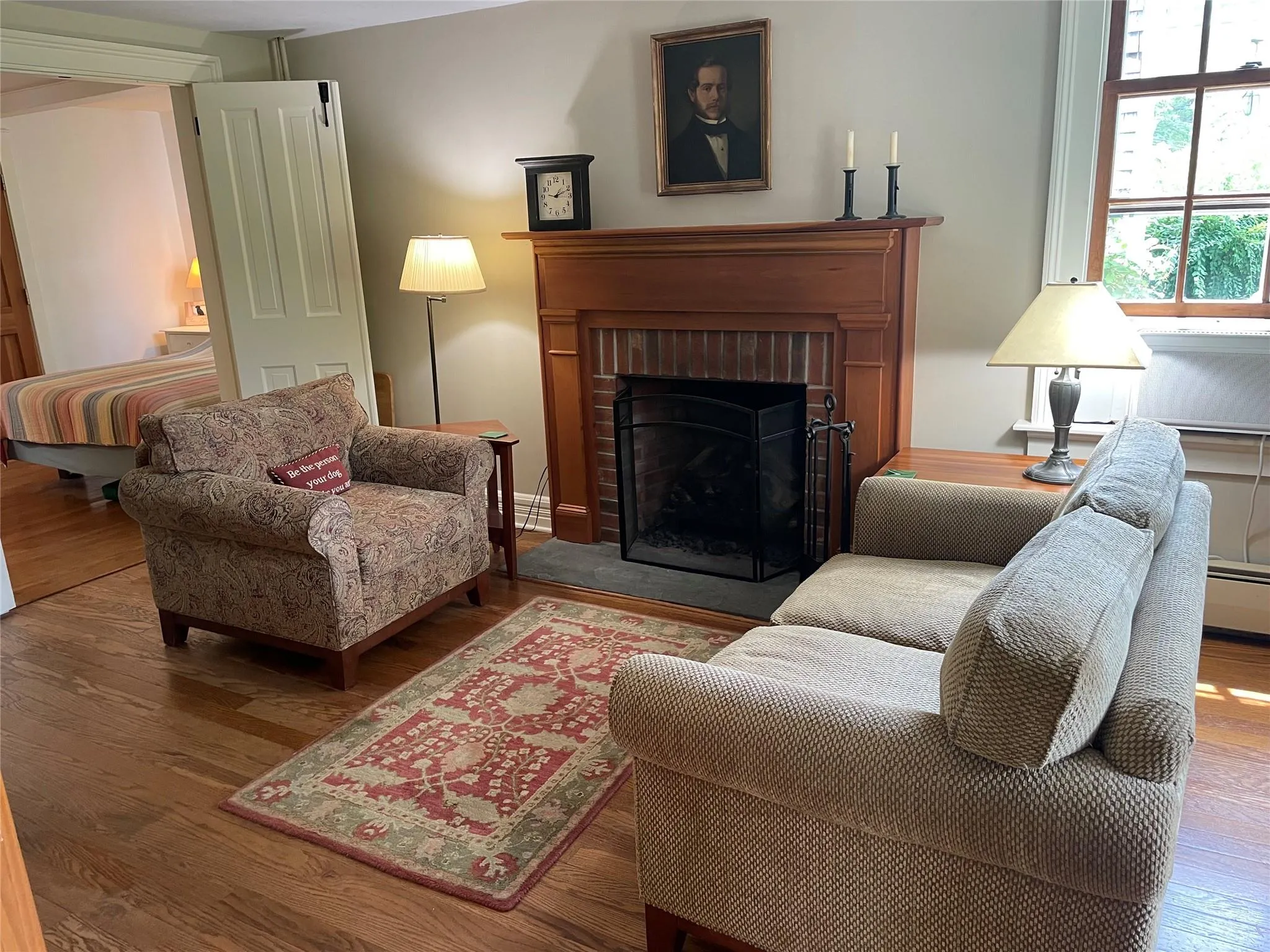 Living room featuring wood finished floors, a brick fireplace, and baseboard heating Living room featuring wood finished floors, a brick fireplace, and baseboard heating