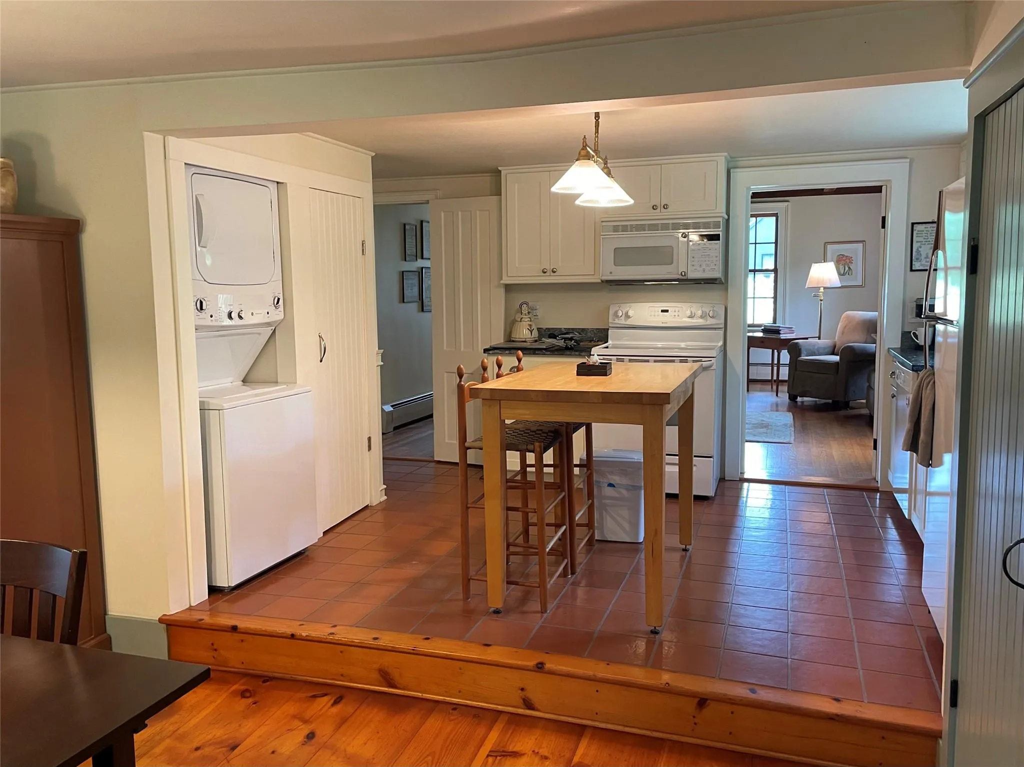 Kitchen with estacked washer and dryer, white appliances, white cabinetry, dark tile patterned floors, and a baseboard radiator Kitchen with estacked washer and dryer, white appliances, white cabinetry, dark tile patterned floors, and a baseboard radiator