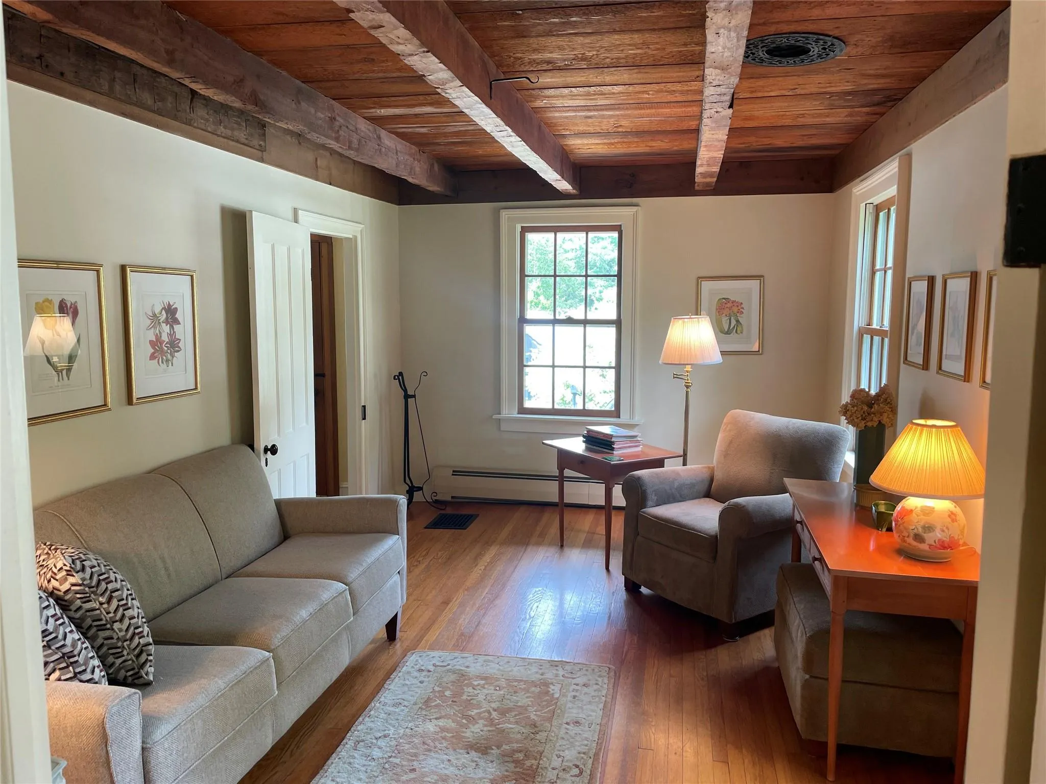 Living room with a wood ceiling with exposed beams, wood finished floors, and baseboard heating Living room with a wood ceiling with exposed beams, wood finished floors, and baseboard heating