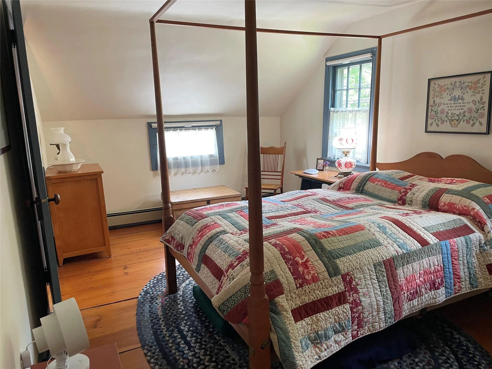 Bedroom featuring light wood-style floors, vaulted ceiling, multiple windows, and a baseboard heating unit Bedroom featuring light wood-style floors, vaulted ceiling, multiple windows, and a baseboard heating unit