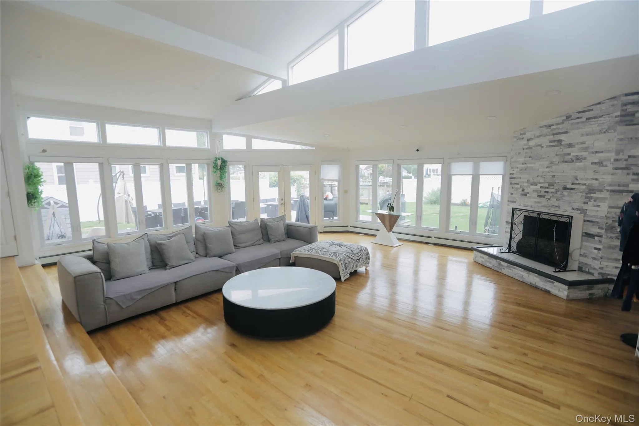 Living area featuring high vaulted ceiling, light wood-style floors, a fireplace, beam ceiling, and a baseboard heating unit Living area featuring high vaulted ceiling, light wood-style floors, a fireplace, beam ceiling, and a baseboard heating unit