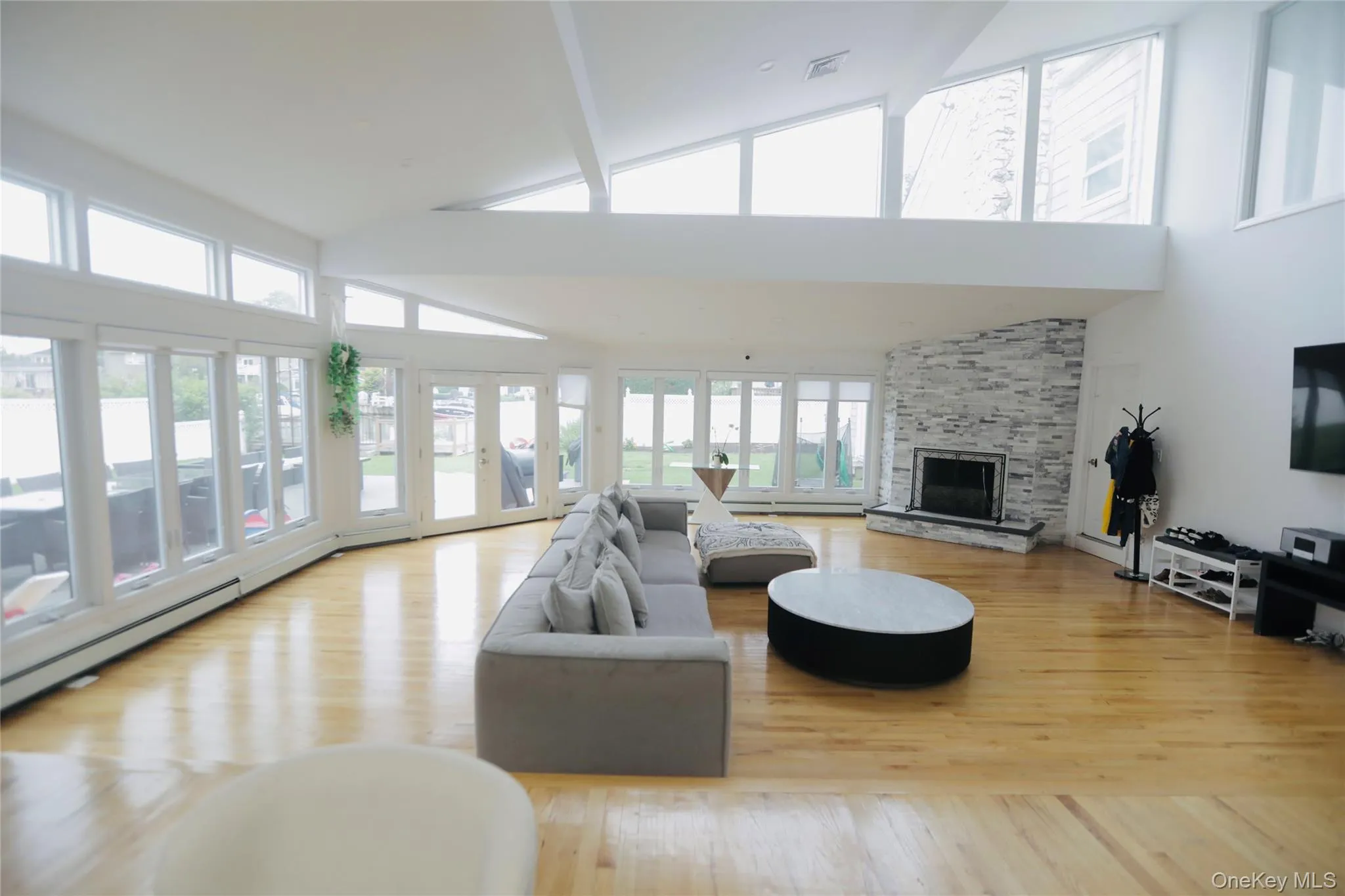 Living area with a stone fireplace, light wood finished floors, and high vaulted ceiling Living area with a stone fireplace, light wood finished floors, and high vaulted ceiling