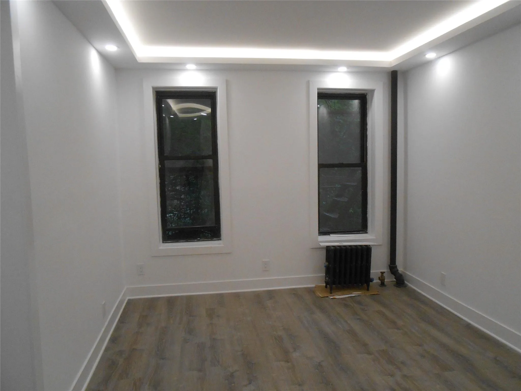 Unfurnished room with radiator heating unit, wood finished floors, recessed lighting, and a tray ceiling Unfurnished room with radiator heating unit, wood finished floors, recessed lighting, and a tray ceiling