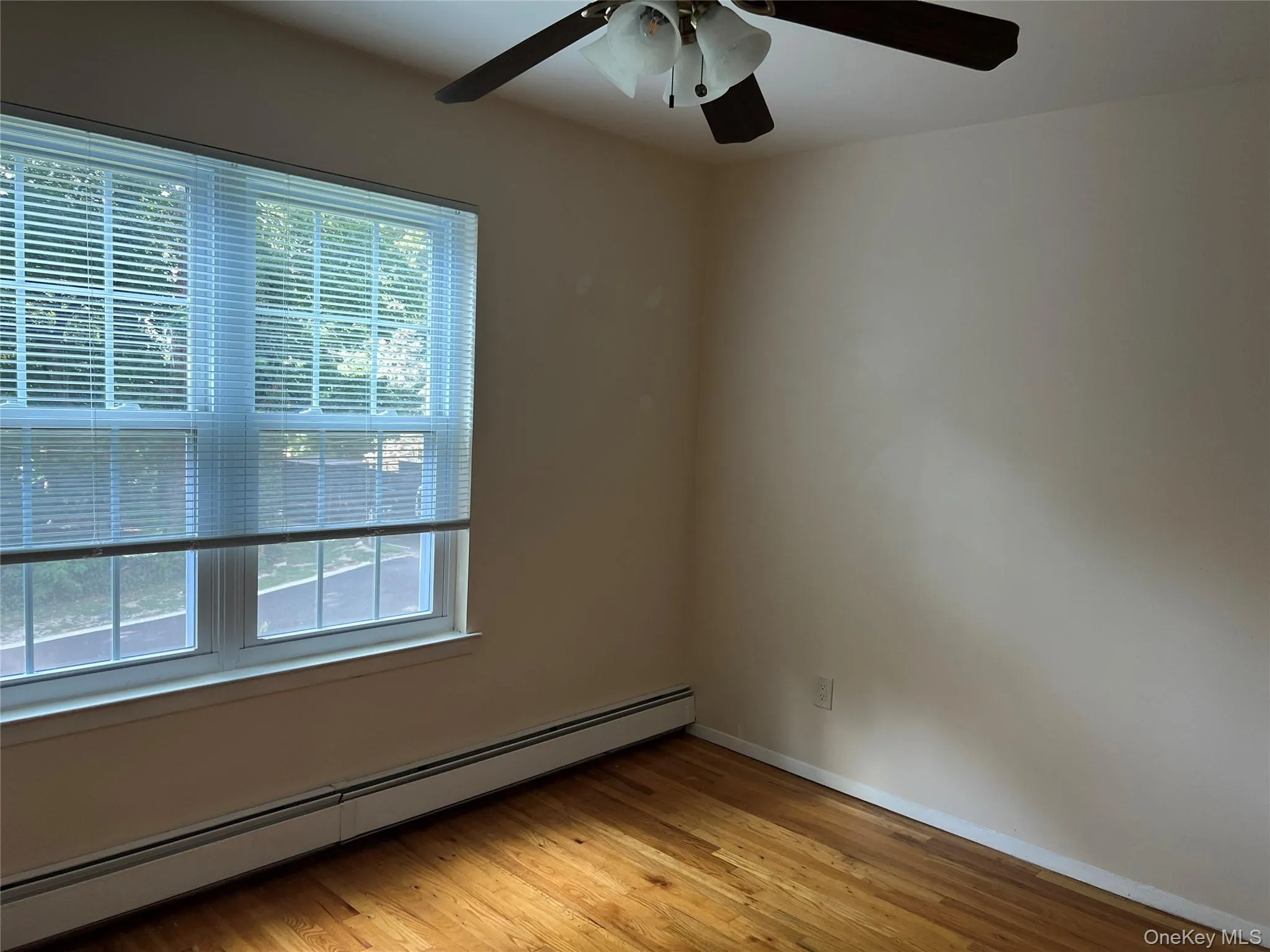 Empty room with baseboard heating, light wood finished floors, and ceiling fan Empty room with baseboard heating, light wood finished floors, and ceiling fan