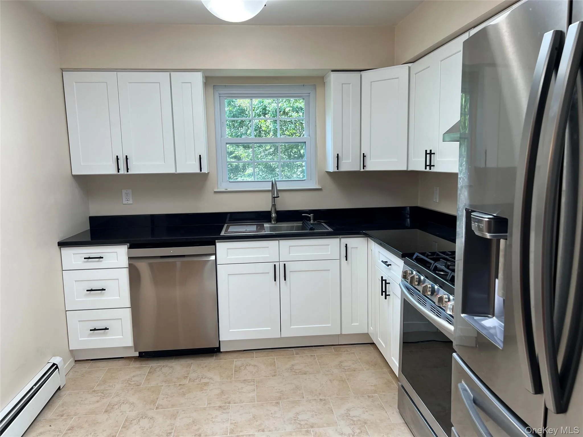 Kitchen with stainless steel appliances, baseboard heating, white cabinets, and granite countertops Kitchen with stainless steel appliances, baseboard heating, white cabinets, and granite countertops