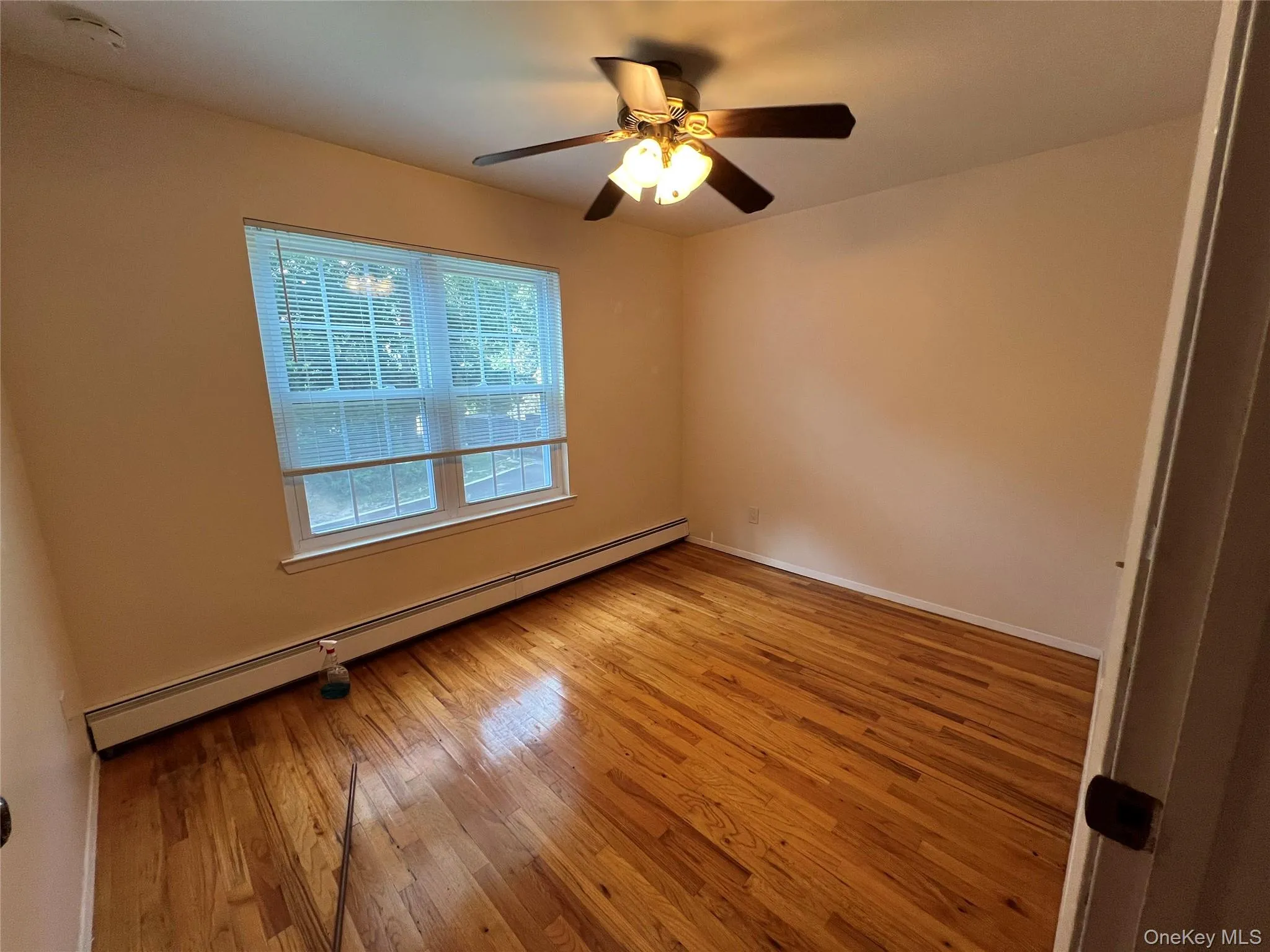 Unfurnished room featuring baseboard heating, light wood finished floors, and ceiling fan Unfurnished room featuring baseboard heating, light wood finished floors, and ceiling fan