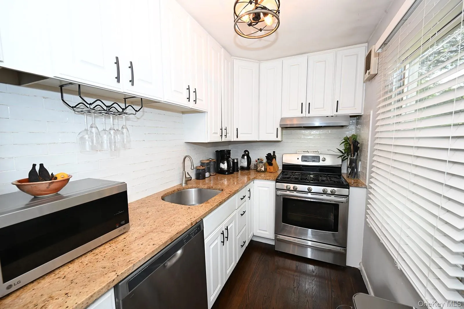 Kitchen with stainless steel appliances, white cabinetry, light stone counters, dark wood-type flooring, and decorative backsplash Kitchen with stainless steel appliances, white cabinetry, light stone counters, dark wood-type flooring, and decorative backsplash