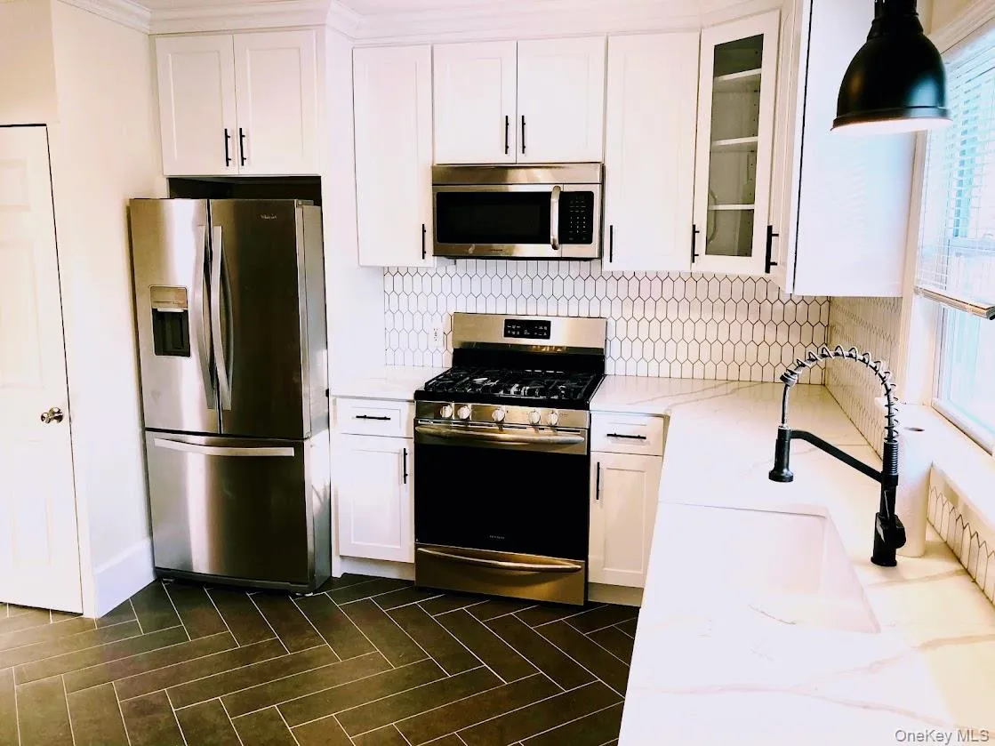 Kitchen featuring appliances with stainless steel finishes, white cabinetry, decorative backsplash, and glass insert cabinets Kitchen featuring appliances with stainless steel finishes, white cabinetry, decorative backsplash, and glass insert cabinets