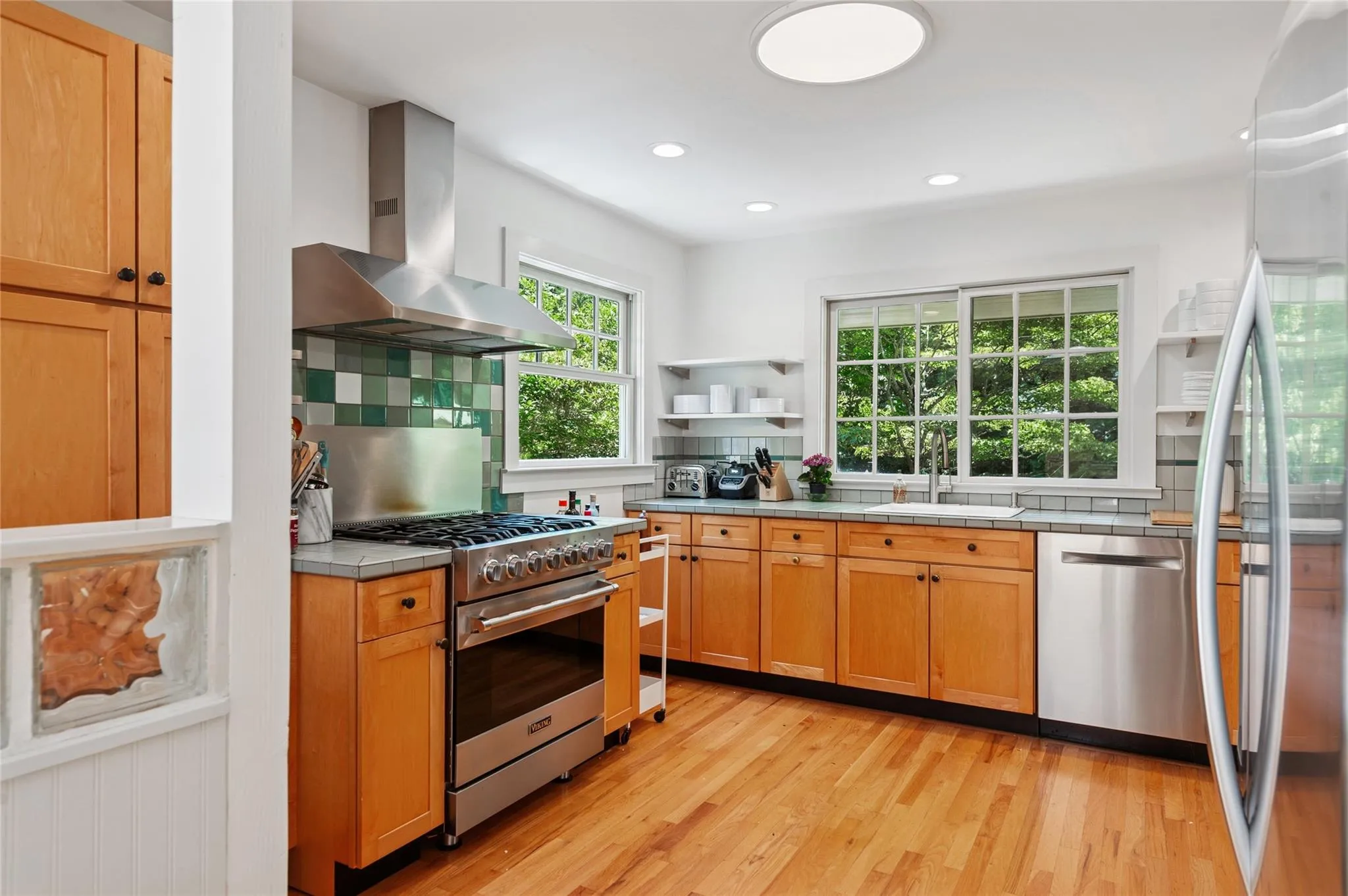 Kitchen with appliances with stainless steel finishes, wall chimney exhaust hood, tile counters, backsplash, and recessed lighting Kitchen with appliances with stainless steel finishes, wall chimney exhaust hood, tile counters, backsplash, and recessed lighting