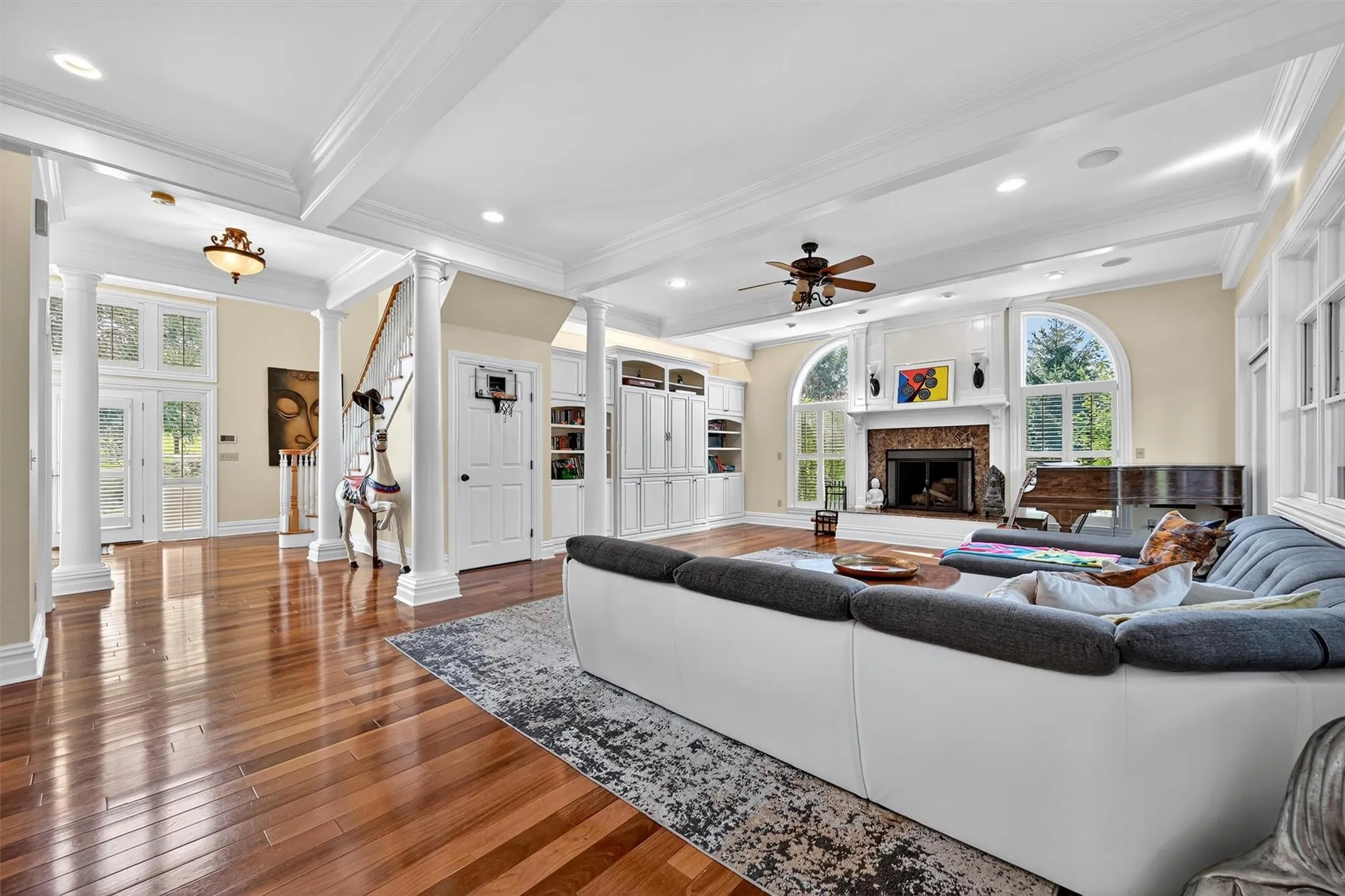 Living area featuring ornate columns, a ceiling fan, a fireplace, wood finished floors, and ornamental molding Living area featuring ornate columns, a ceiling fan, a fireplace, wood finished floors, and ornamental molding