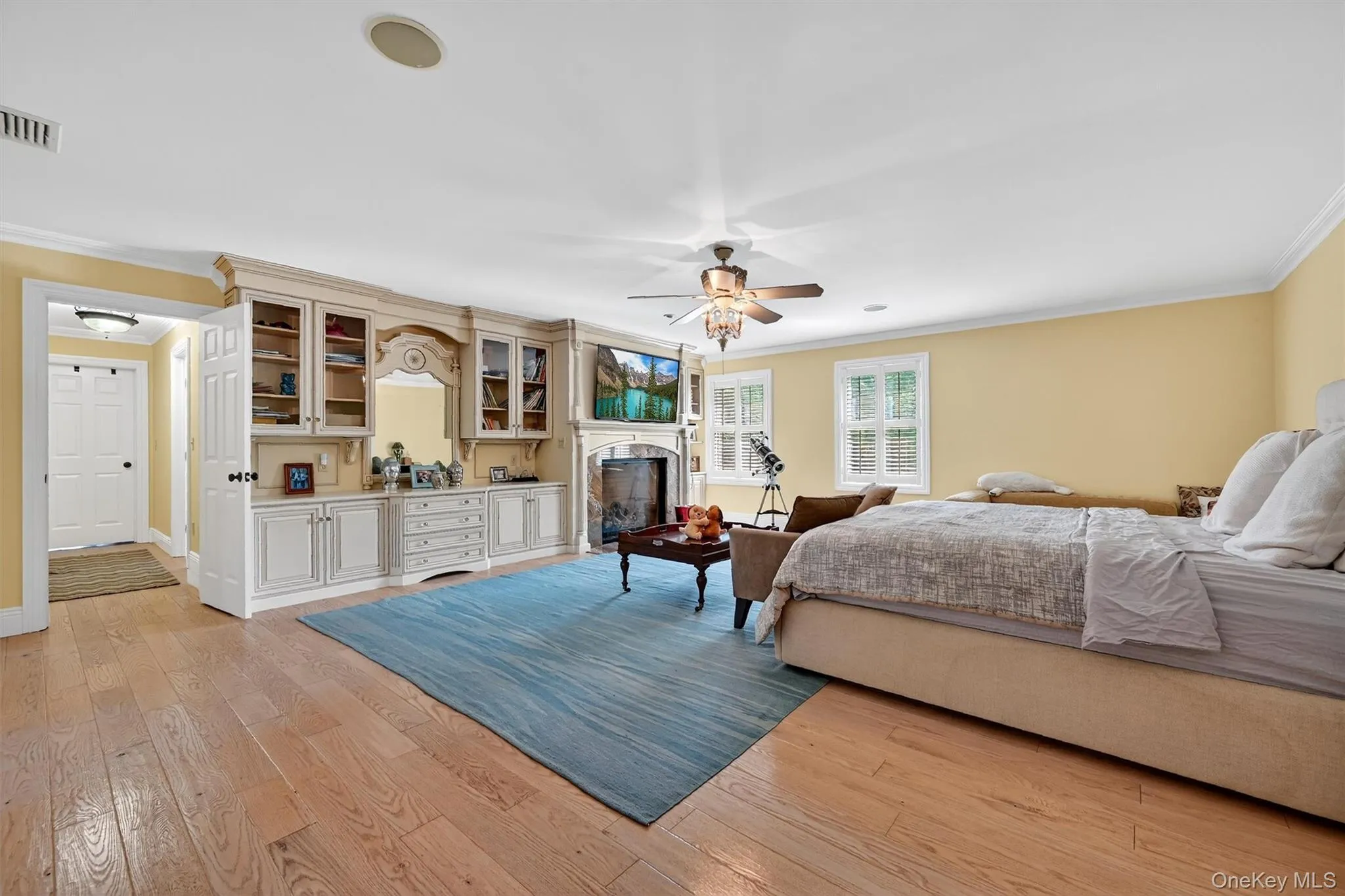 Bedroom with ornamental molding, light wood-style flooring, a fireplace, and a ceiling fan Bedroom with ornamental molding, light wood-style flooring, a fireplace, and a ceiling fan
