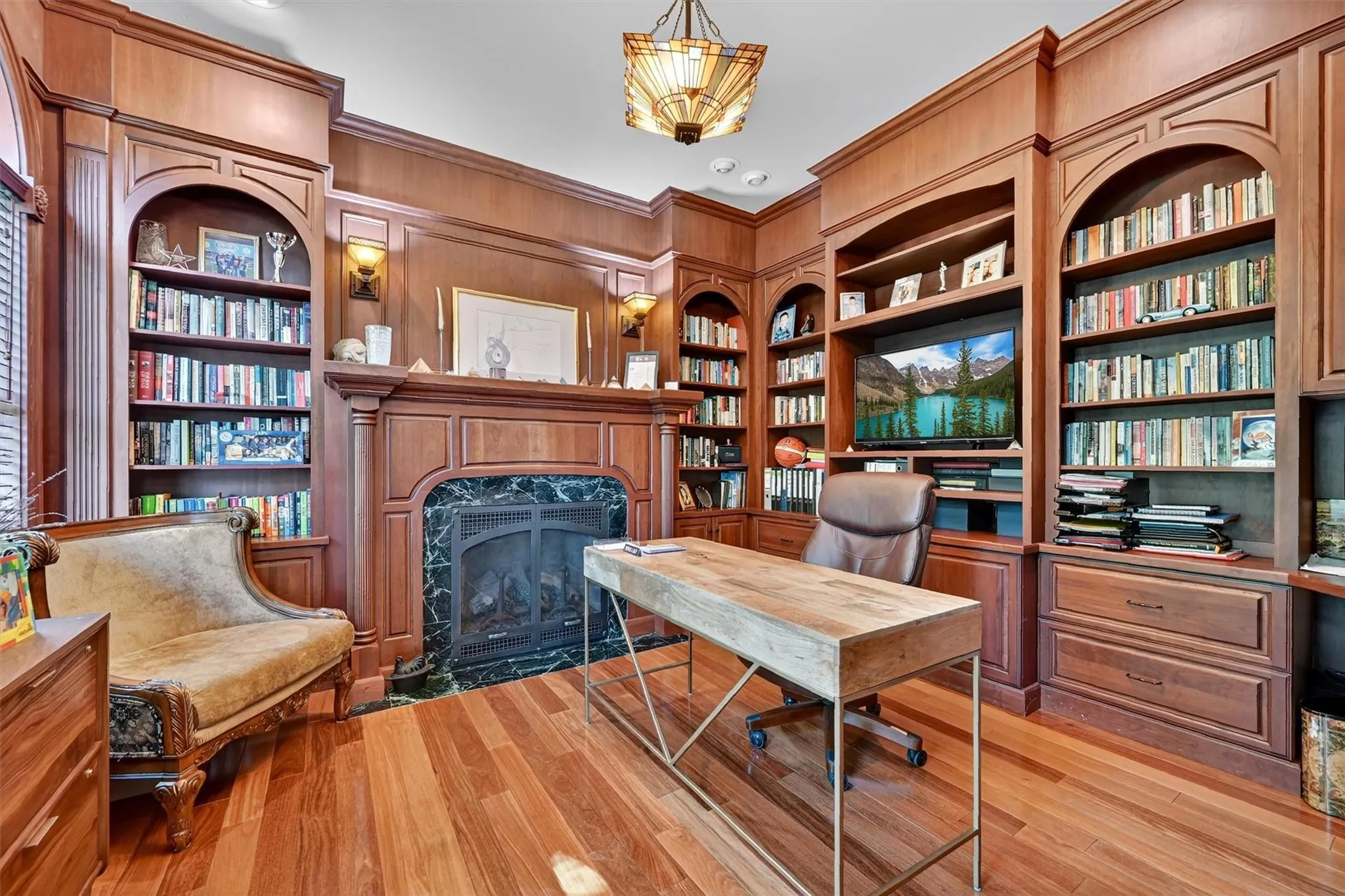 Home office with a high end fireplace, ornamental molding, built in features, light wood-style flooring, and wooden walls Home office with a high end fireplace, ornamental molding, built in features, light wood-style flooring, and wooden walls