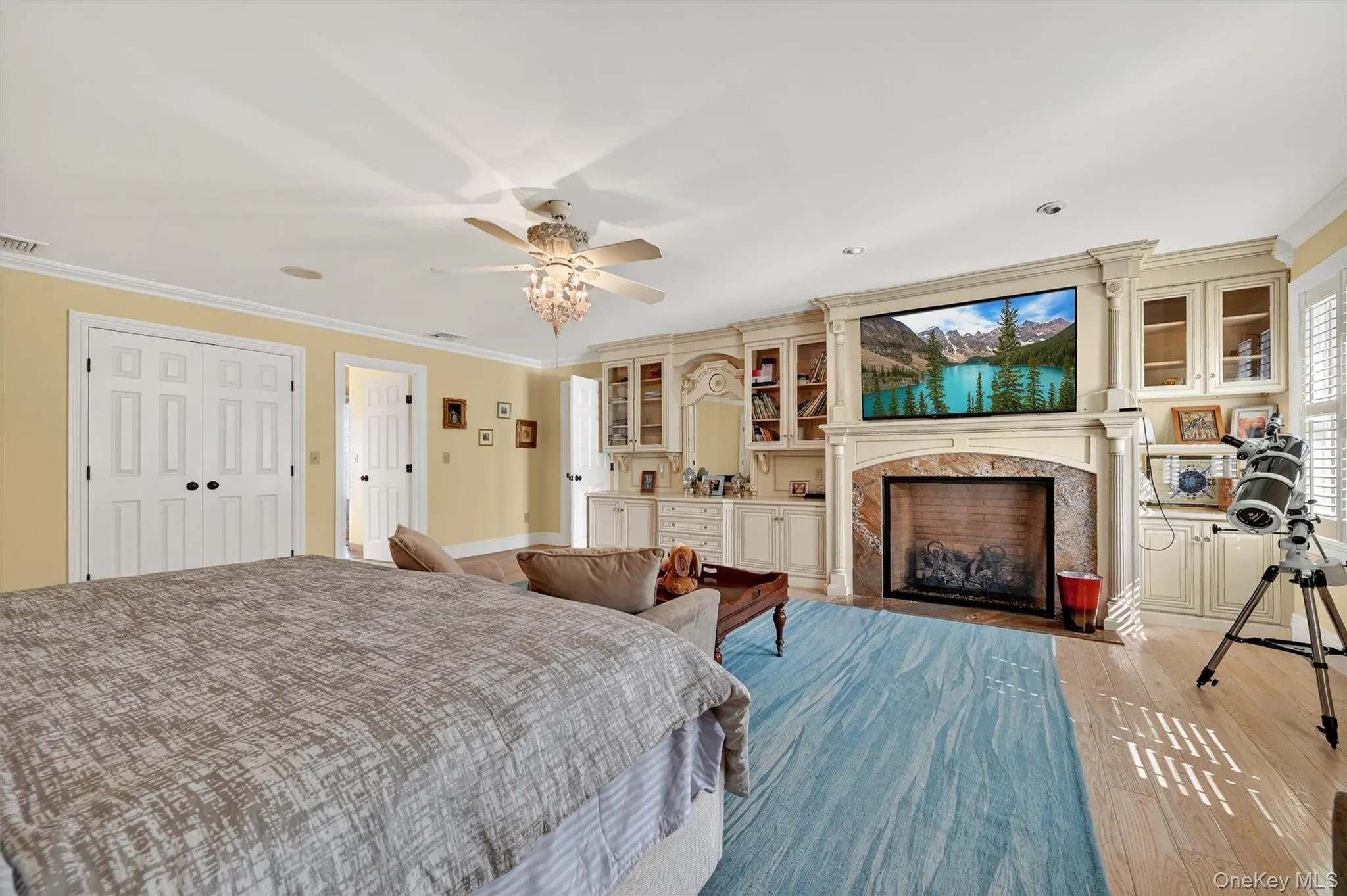 Bedroom with a high end fireplace, light wood-type flooring, ornamental molding, and a ceiling fan Bedroom with a high end fireplace, light wood-type flooring, ornamental molding, and a ceiling fan