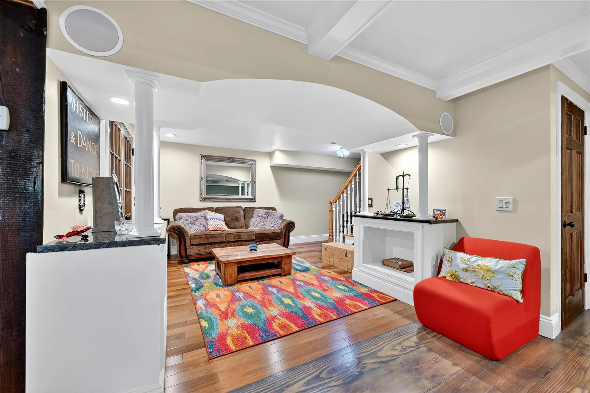 Living room featuring decorative columns, stairs, wood finished floors, crown molding, and beamed ceiling Living room featuring decorative columns, stairs, wood finished floors, crown molding, and beamed ceiling