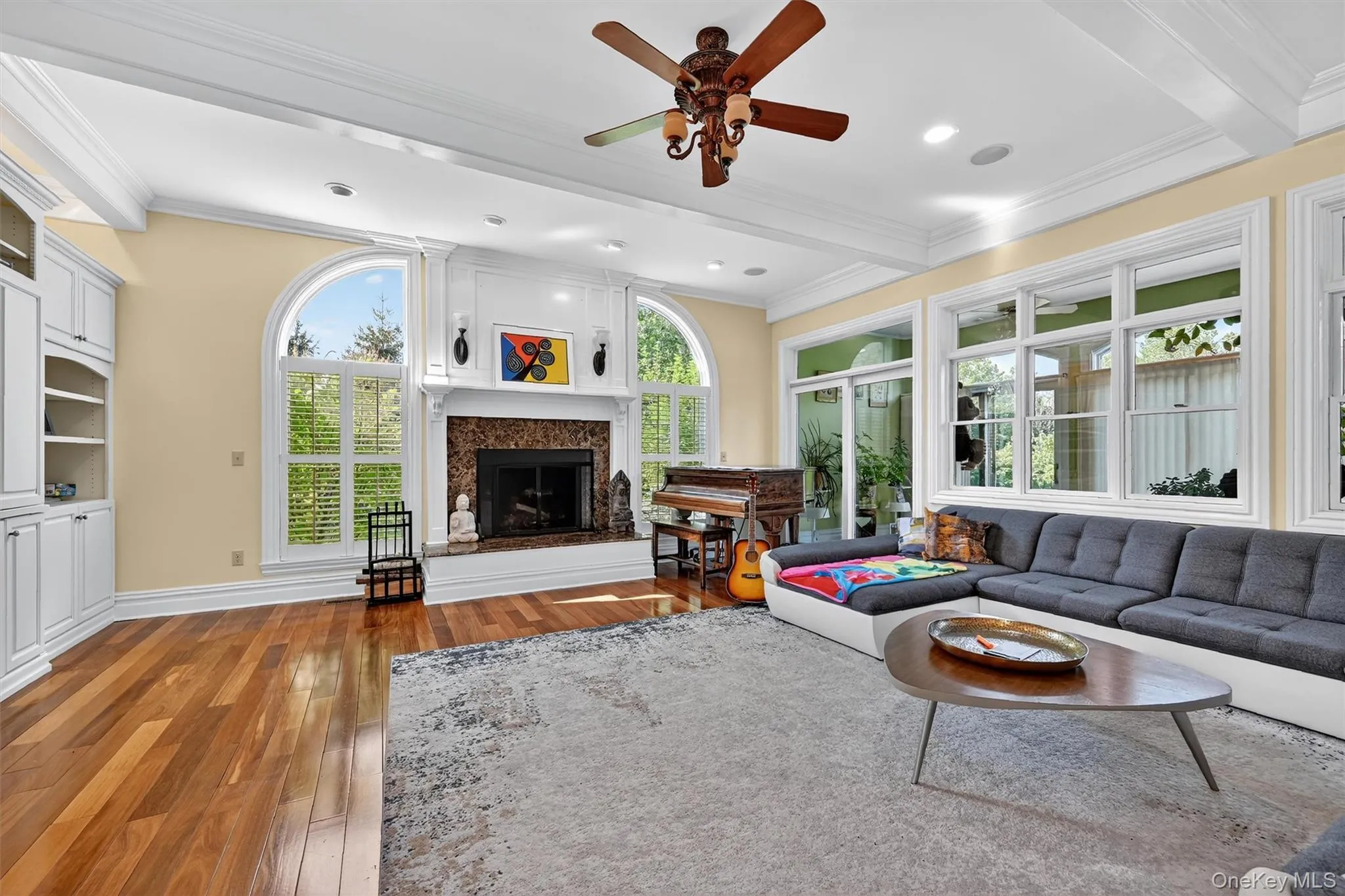 Living area featuring light wood-style flooring, a fireplace with raised hearth, a ceiling fan, ornamental molding, and recessed lighting Living area featuring light wood-style flooring, a fireplace with raised hearth, a ceiling fan, ornamental molding, and recessed lighting
