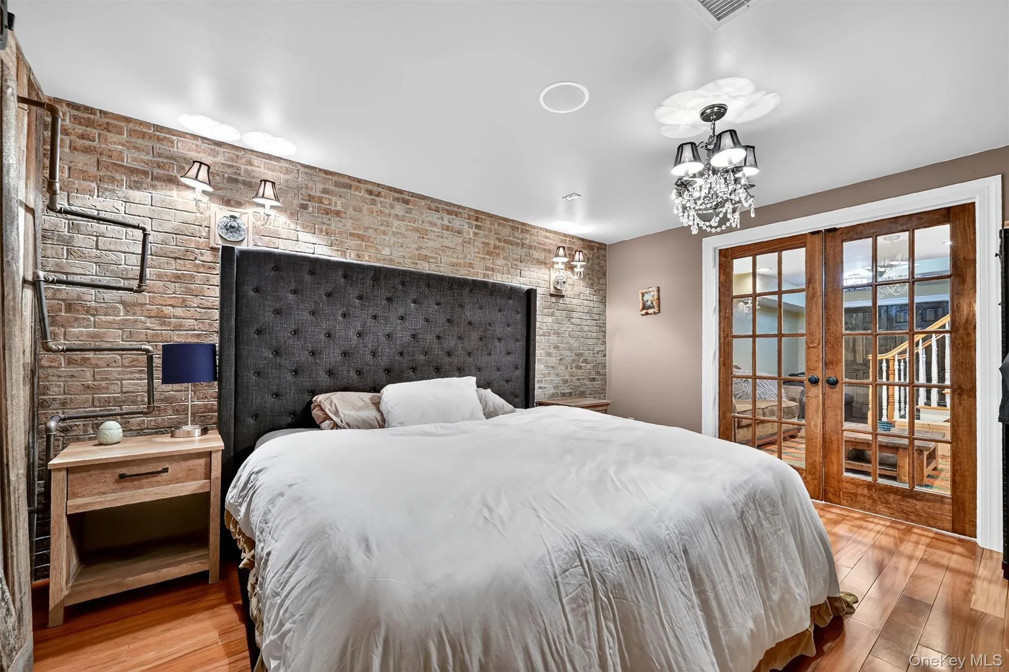 Bedroom with brick wall, light wood-style flooring, french doors, a chandelier, and access to exterior Bedroom with brick wall, light wood-style flooring, french doors, a chandelier, and access to exterior