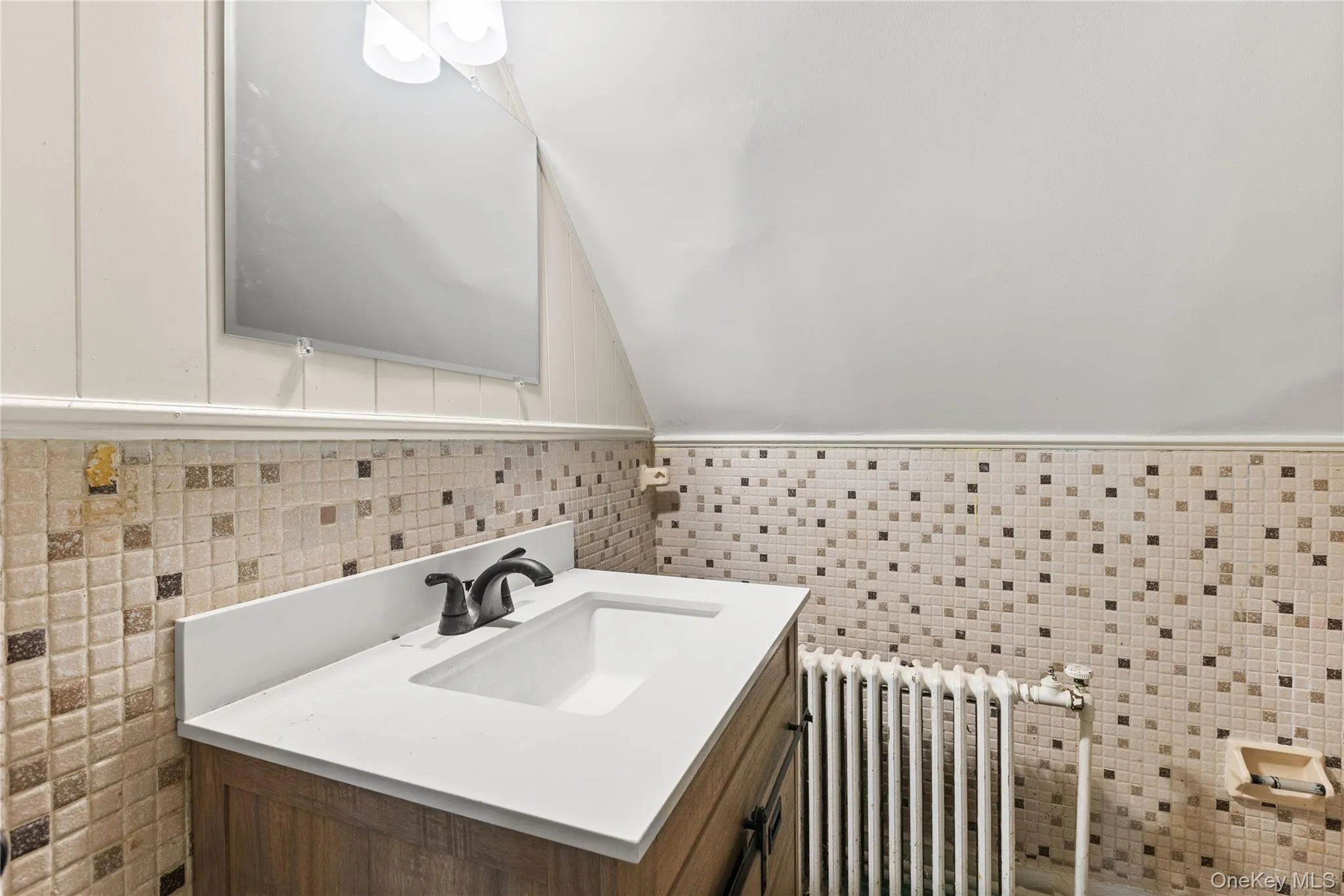 Bathroom with radiator heating unit, lofted ceiling, vanity, and tile walls Bathroom with radiator heating unit, lofted ceiling, vanity, and tile walls