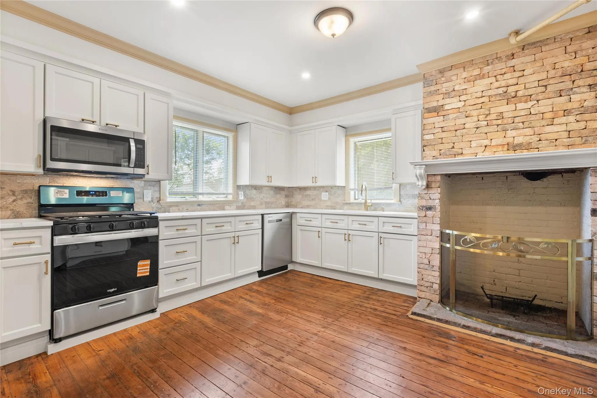 Kitchen featuring dark wood finished floors, appliances with stainless steel finishes, white cabinetry, decorative backsplash, and crown molding Kitchen featuring dark wood finished floors, appliances with stainless steel finishes, white cabinetry, decorative backsplash, and crown molding