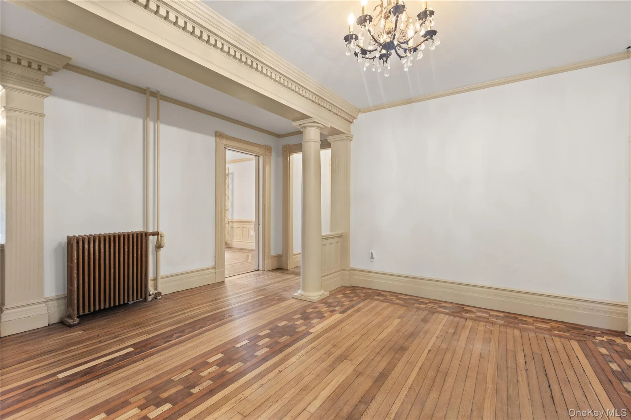 Empty room featuring crown molding, wood-type flooring, radiator heating unit, and a chandelier Empty room featuring crown molding, wood-type flooring, radiator heating unit, and a chandelier