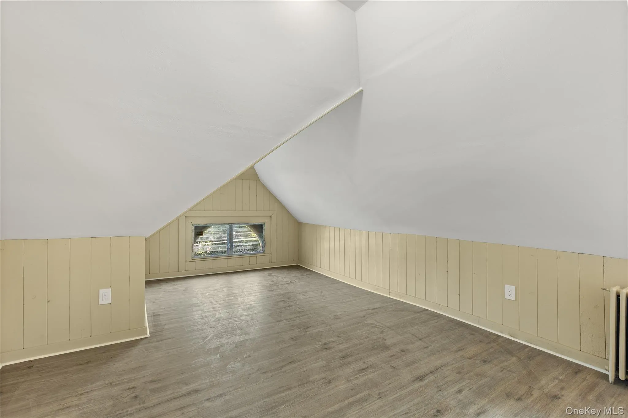 Additional living space featuring wood walls, wood finished floors, vaulted ceiling, and radiator heating unit Additional living space featuring wood walls, wood finished floors, vaulted ceiling, and radiator heating unit