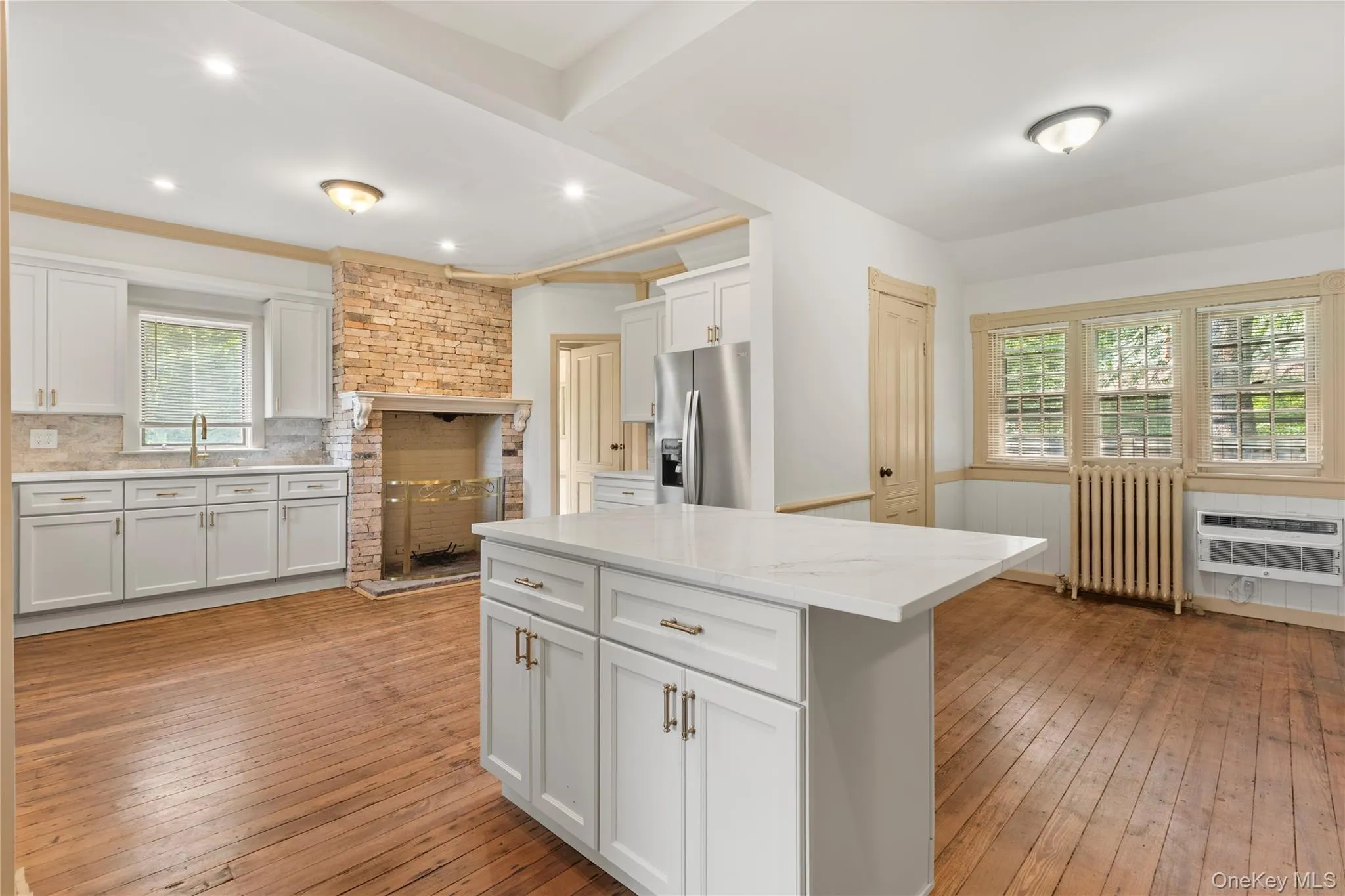 Kitchen with light wood-type flooring, a center island, radiator heating unit, white cabinetry, and a wainscoted wall Kitchen with light wood-type flooring, a center island, radiator heating unit, white cabinetry, and a wainscoted wall