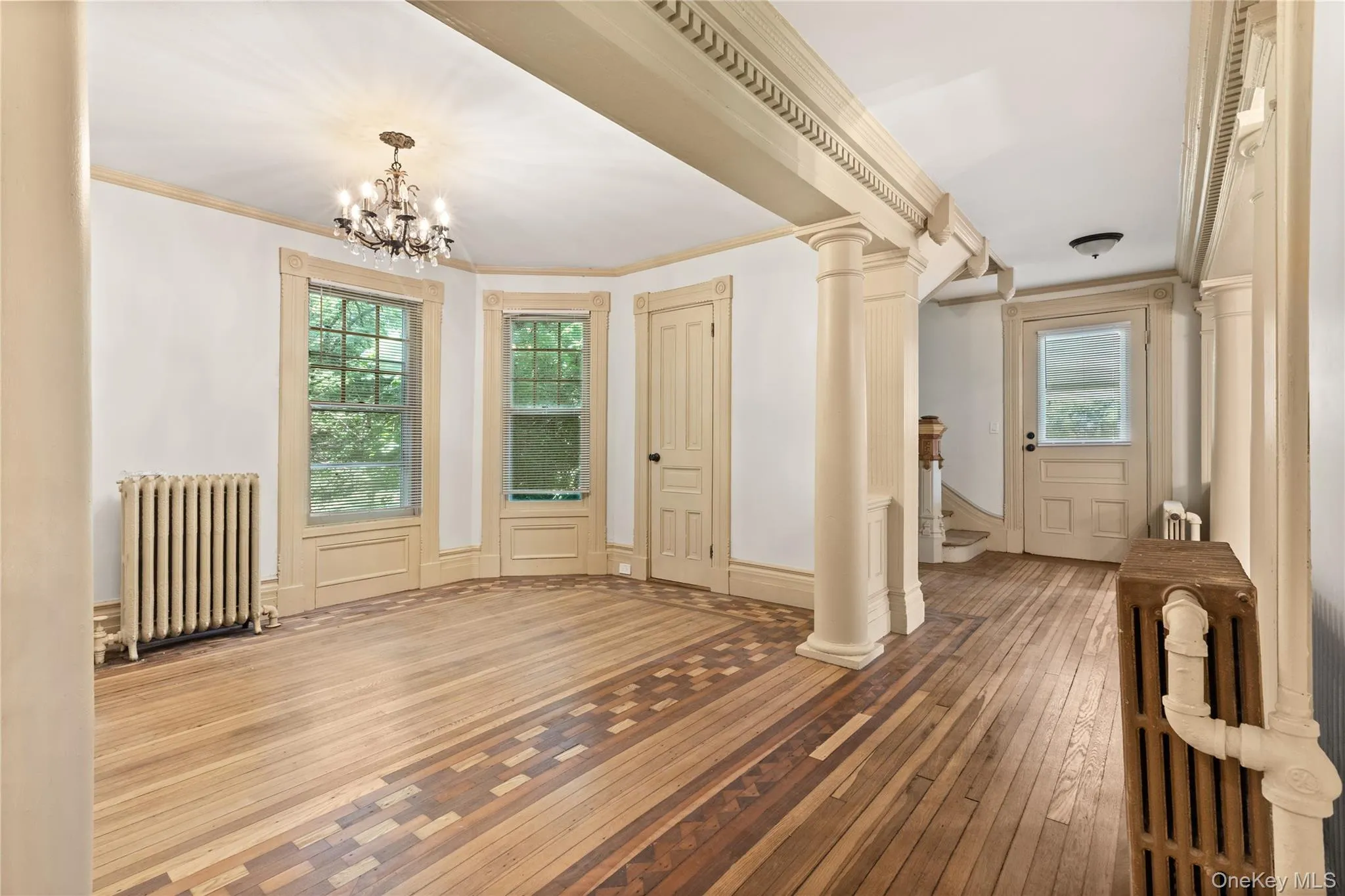 Unfurnished dining area with radiator, hardwood / wood-style floors, ornamental molding, and a chandelier Unfurnished dining area with radiator, hardwood / wood-style floors, ornamental molding, and a chandelier