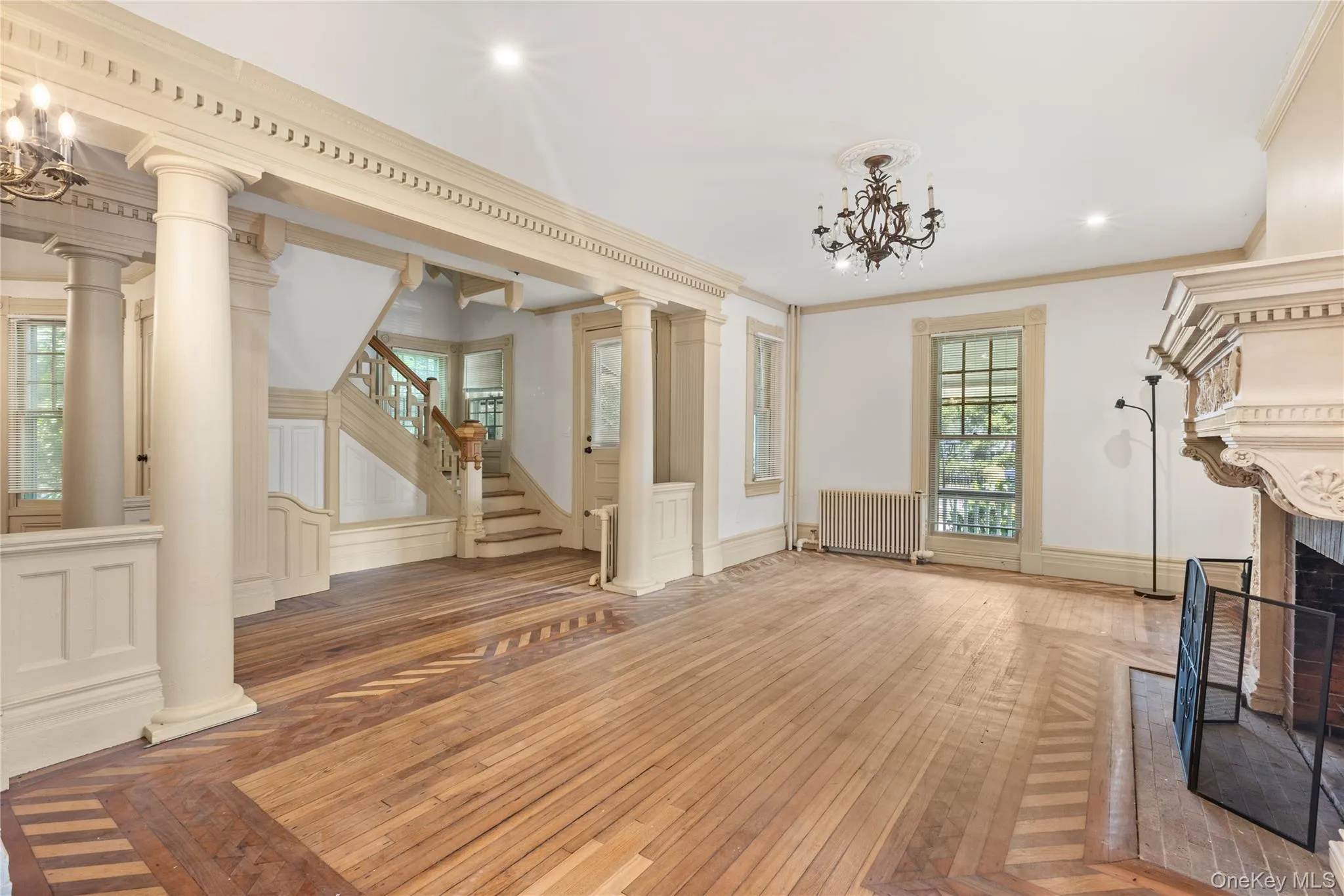 Unfurnished living room with a chandelier, hardwood / wood-style floors, crown molding, a fireplace, and radiator heating unit Unfurnished living room with a chandelier, hardwood / wood-style floors, crown molding, a fireplace, and radiator heating unit