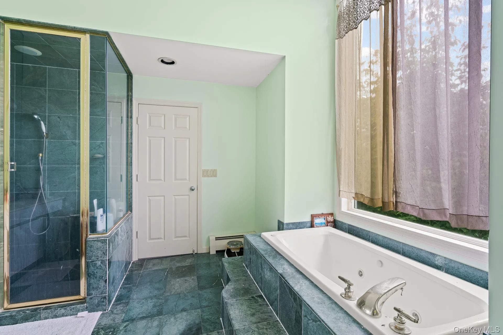 Bathroom featuring a stall shower, a tub with jets, baseboard heating, and dark stone finish floors Bathroom featuring a stall shower, a tub with jets, baseboard heating, and dark stone finish floors