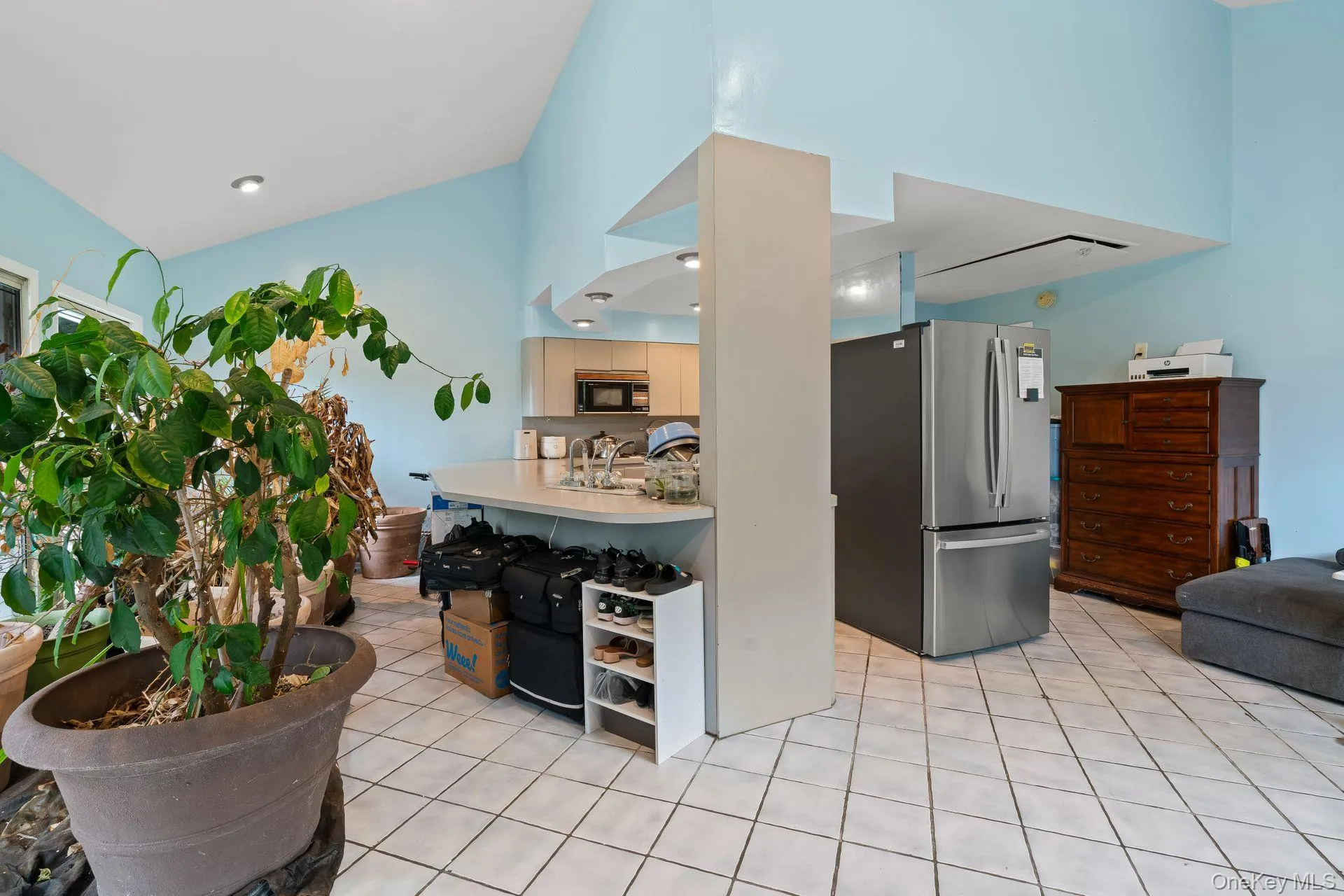 Kitchen featuring freestanding refrigerator, light countertops, light tile patterned floors, black microwave, and open floor plan Kitchen featuring freestanding refrigerator, light countertops, light tile patterned floors, black microwave, and open floor plan