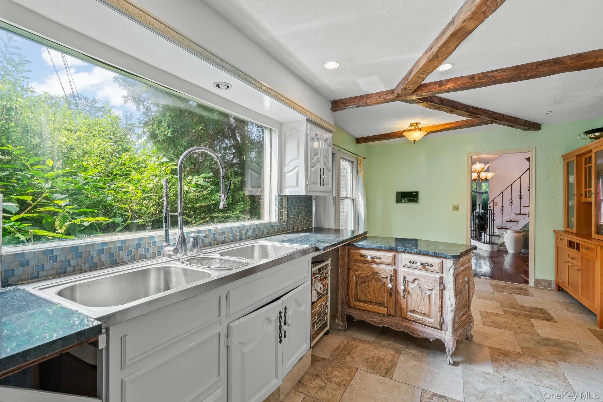 Kitchen featuring backsplash, beamed ceiling, dark stone countertops, a chandelier, and white cabinets Kitchen featuring backsplash, beamed ceiling, dark stone countertops, a chandelier, and white cabinets