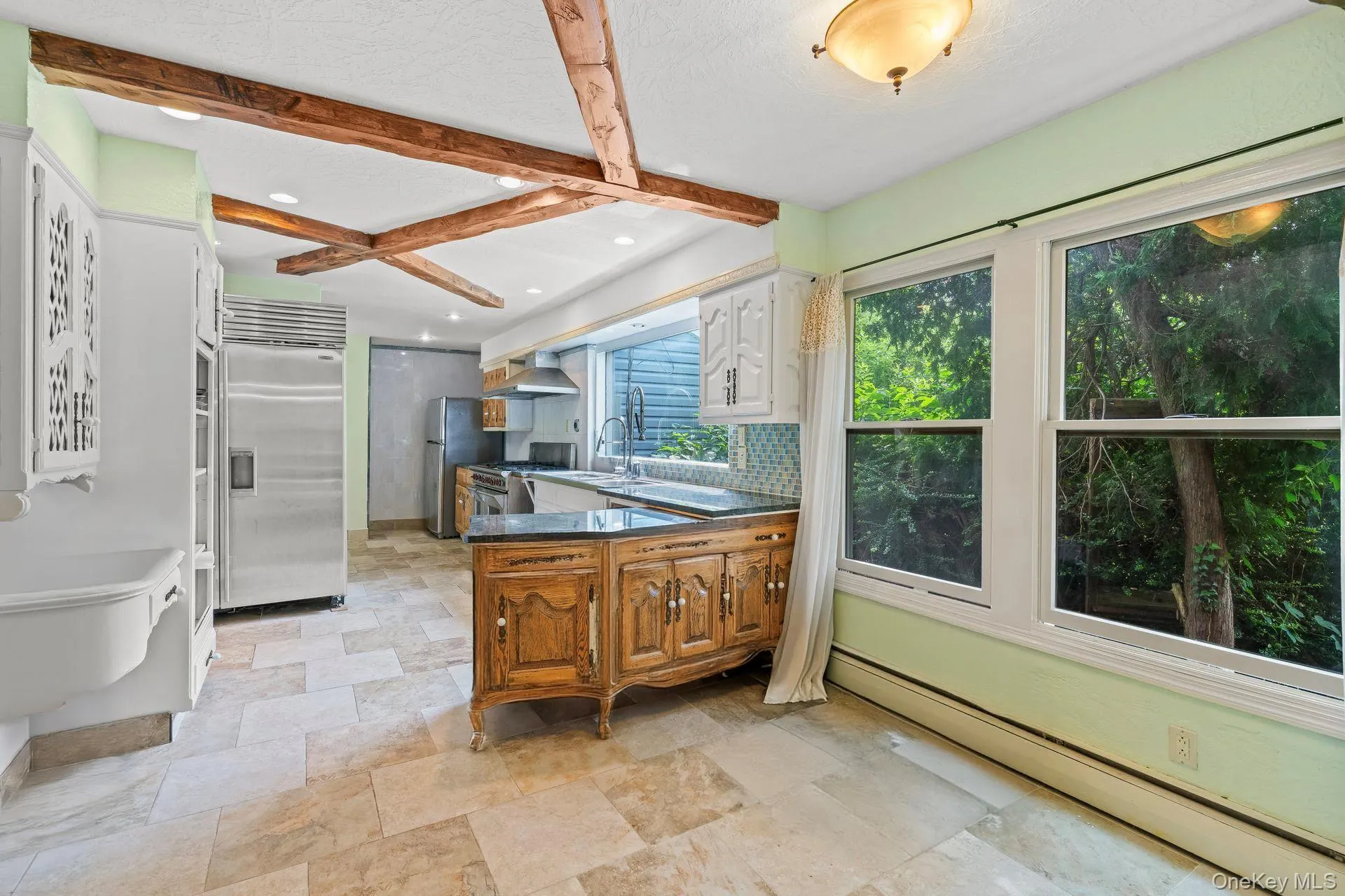 Kitchen with a peninsula, a baseboard heating unit, beamed ceiling, appliances with stainless steel finishes, and tasteful backsplash Kitchen with a peninsula, a baseboard heating unit, beamed ceiling, appliances with stainless steel finishes, and tasteful backsplash