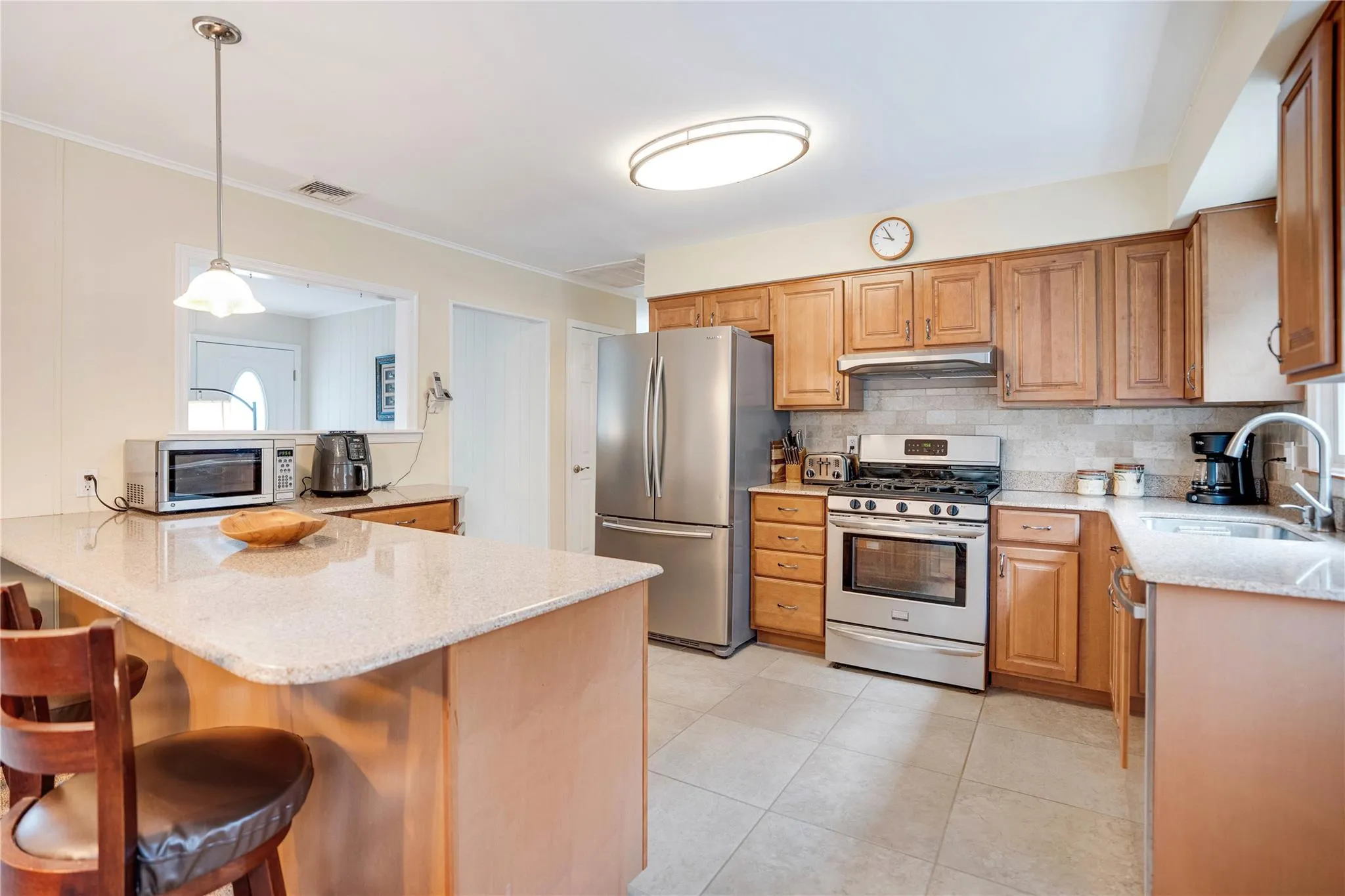 Kitchen featuring appliances with stainless steel finishes, light stone counters, a kitchen breakfast bar, a peninsula, and backsplash