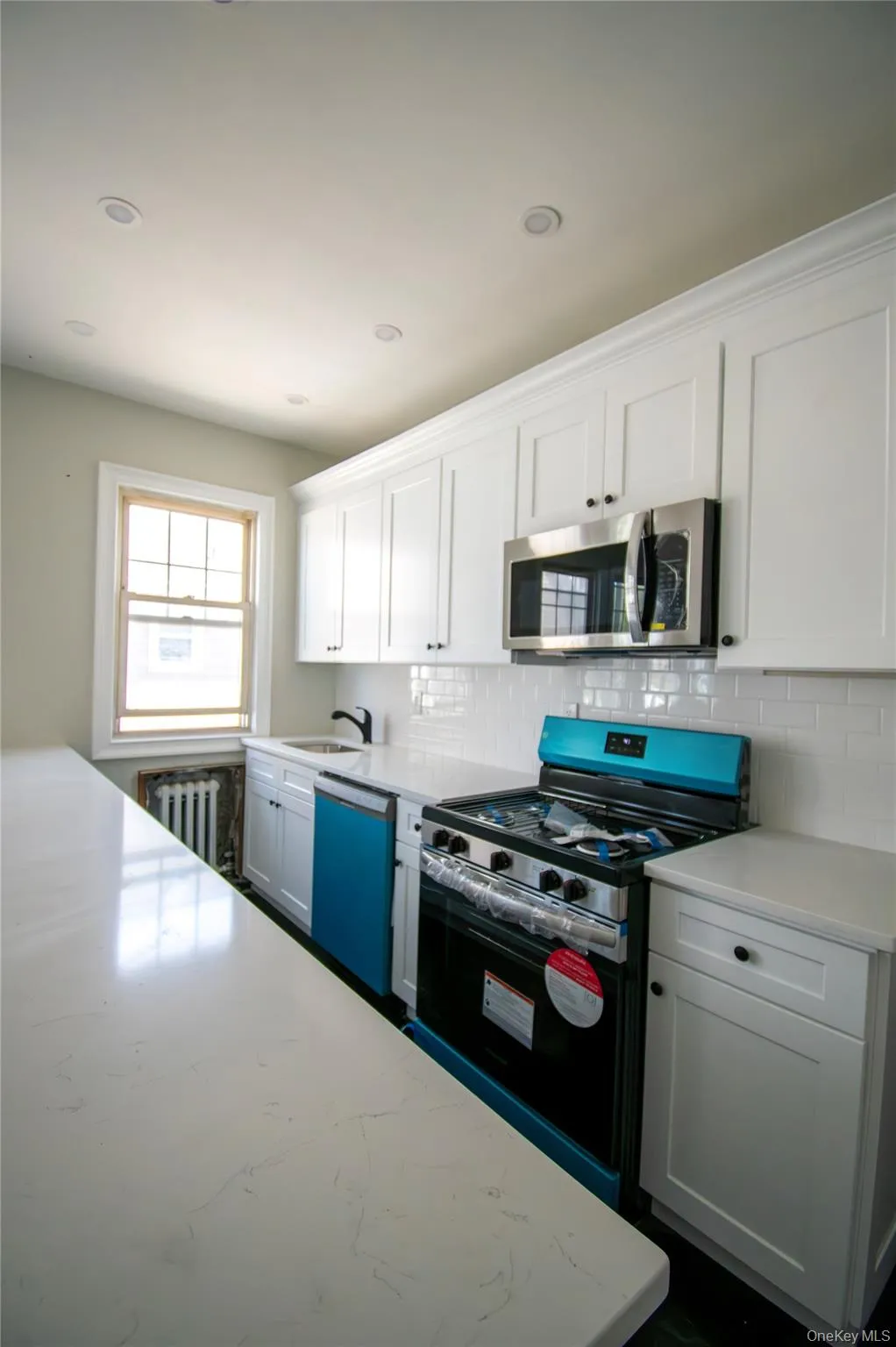 Kitchen featuring stainless steel appliances, tasteful backsplash, white cabinets, radiator heating unit, and recessed lighting Kitchen featuring stainless steel appliances, tasteful backsplash, white cabinets, radiator heating unit, and recessed lighting