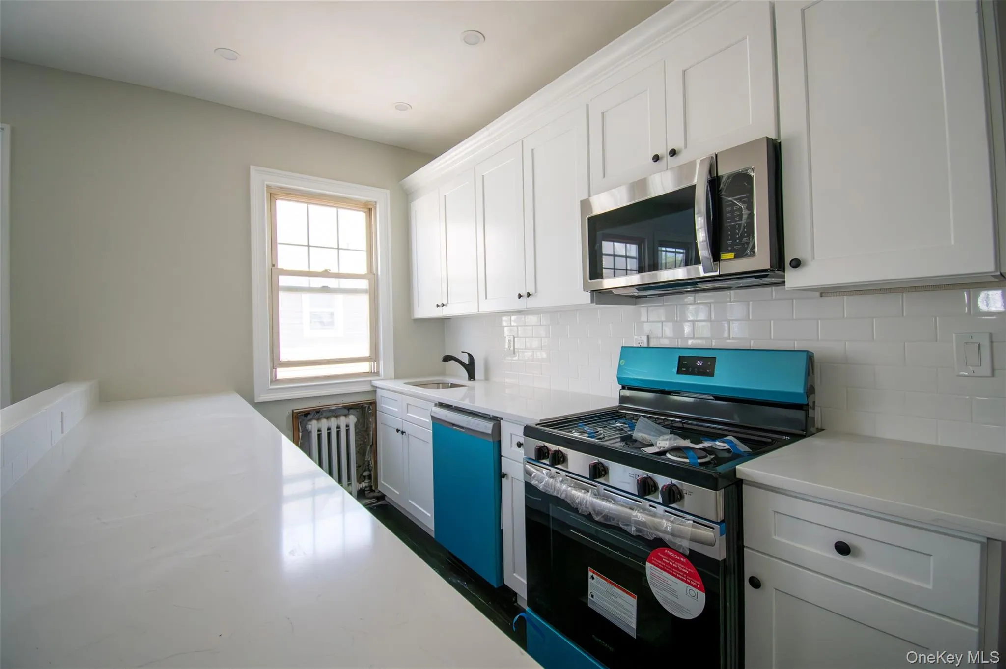 Kitchen with stainless steel appliances, tasteful backsplash, white cabinetry, and radiator heating unit Kitchen with stainless steel appliances, tasteful backsplash, white cabinetry, and radiator heating unit