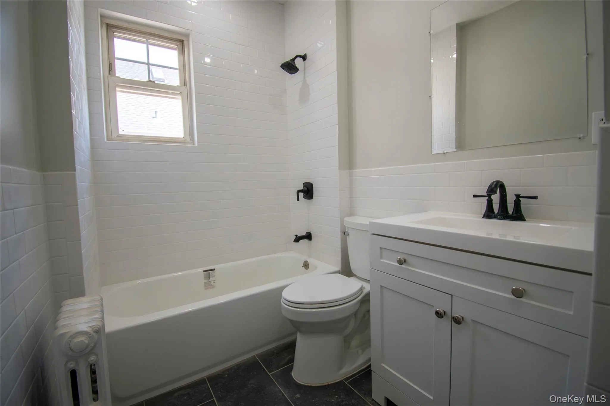 Bathroom featuring tile walls, radiator, vanity, bathtub / shower combination, and tile patterned flooring Bathroom featuring tile walls, radiator, vanity, bathtub / shower combination, and tile patterned flooring