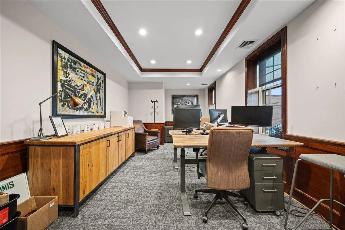 Office space featuring dark carpet, a raised ceiling, ornamental molding, and wooden walls Office space featuring dark carpet, a raised ceiling, ornamental molding, and wooden walls