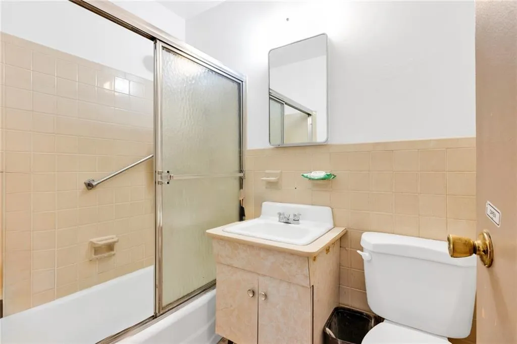 Bathroom with tile walls, shower / bath combination with glass door, vanity, and wainscoting Bathroom with tile walls, shower / bath combination with glass door, vanity, and wainscoting