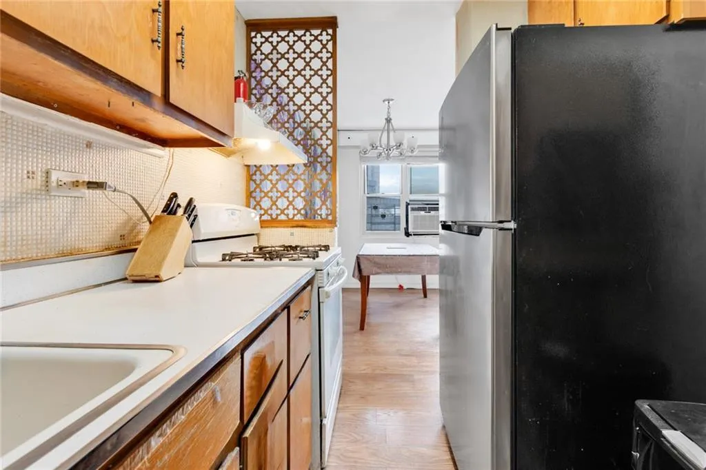 Kitchen with freestanding refrigerator, white range with gas cooktop, light wood-style flooring, light countertops, and under cabinet range hood Kitchen with freestanding refrigerator, white range with gas cooktop, light wood-style flooring, light countertops, and under cabinet range hood