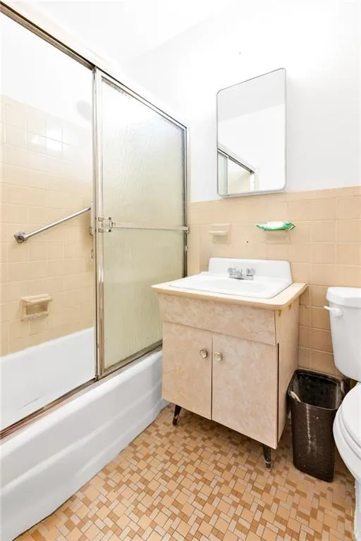 Bathroom featuring vanity, enclosed tub / shower combo, tile walls, and a wainscoted wall Bathroom featuring vanity, enclosed tub / shower combo, tile walls, and a wainscoted wall