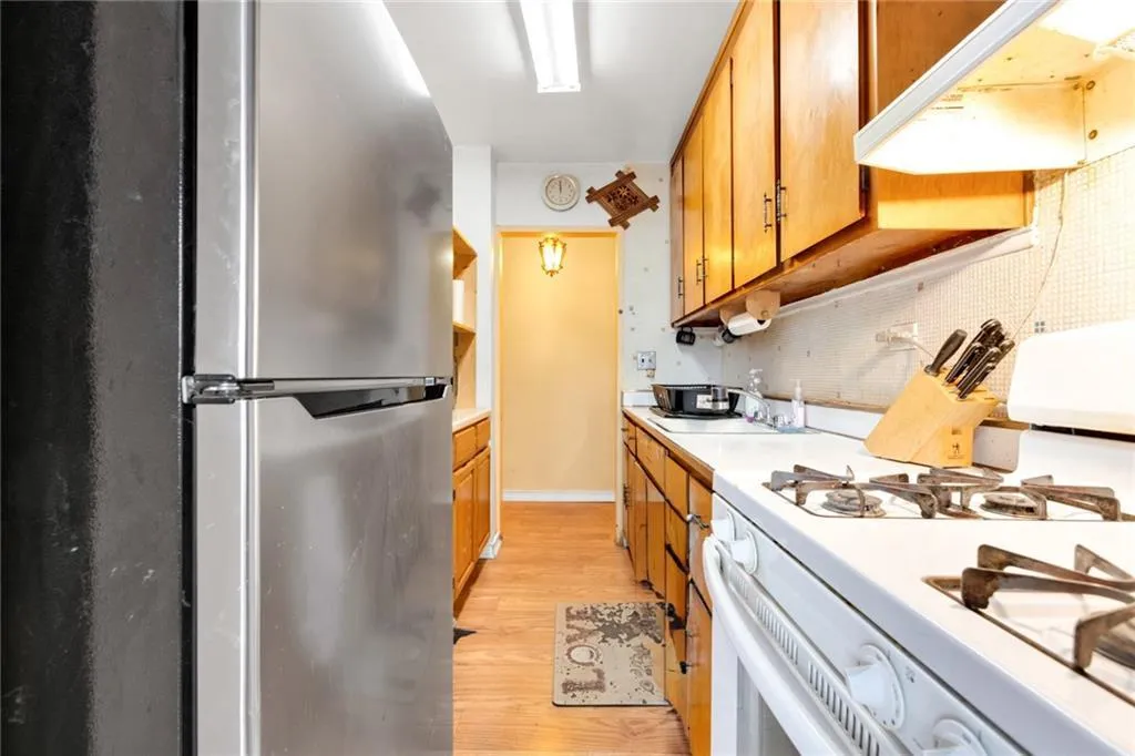 Kitchen featuring freestanding refrigerator, white gas range oven, exhaust hood, light countertops, and light wood-type flooring Kitchen featuring freestanding refrigerator, white gas range oven, exhaust hood, light countertops, and light wood-type flooring